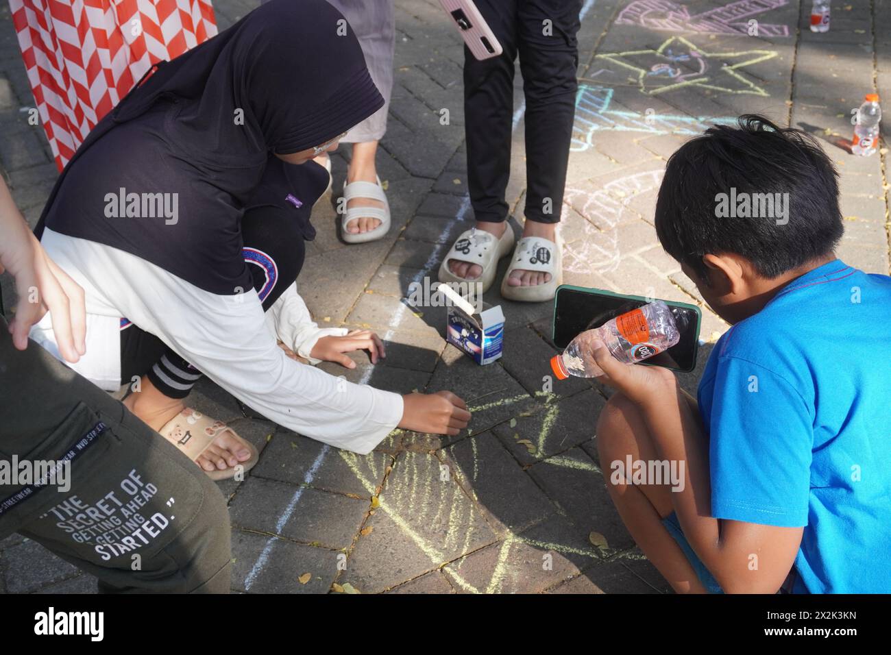 Bambini che disegnano su blocchi di pavimentazione usando il gesso per segnare l'inizio della corsa per commemorare il giorno dell'indipendenza dell'Indonesia Foto Stock