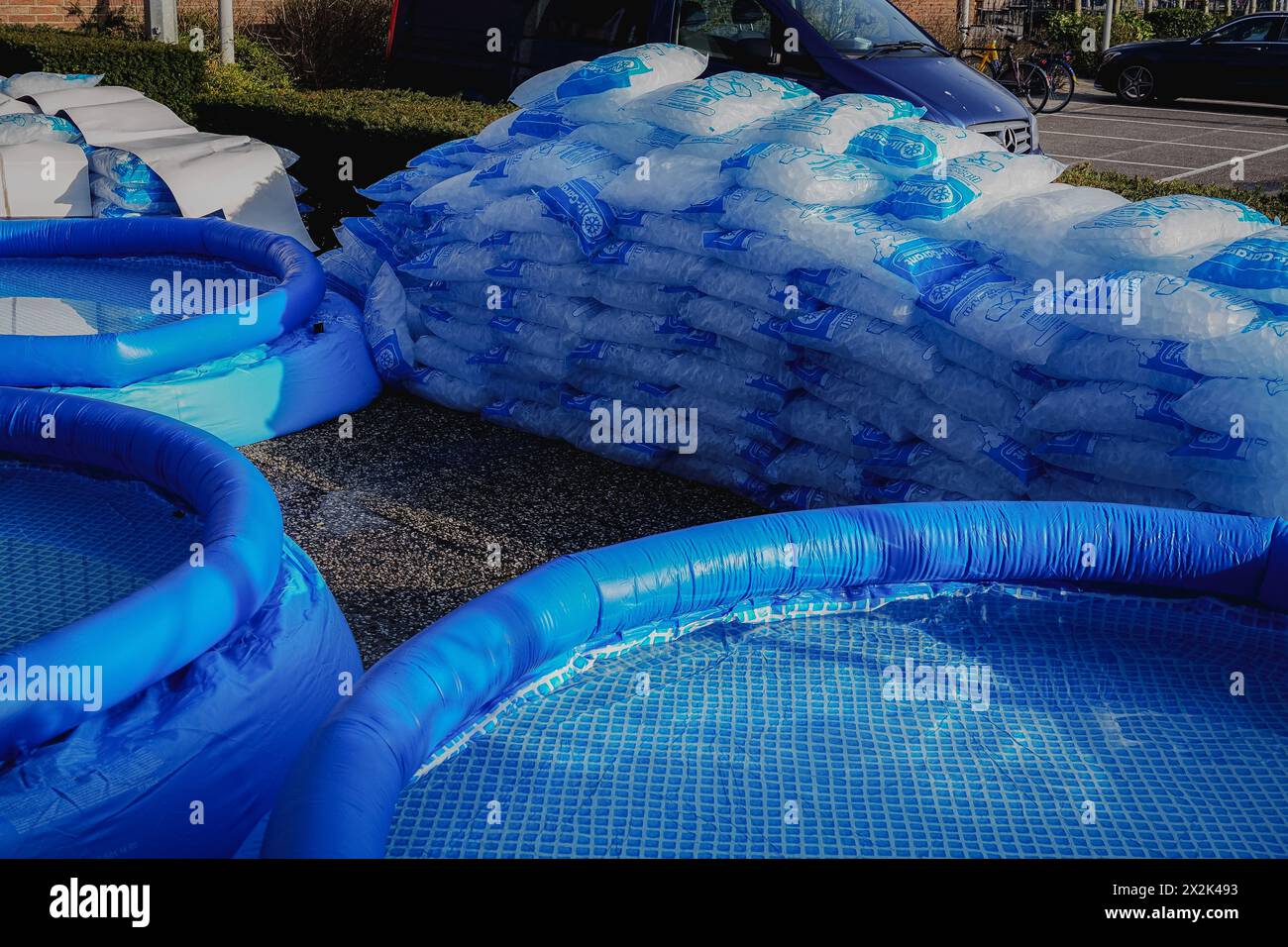 Più piscine gonfiabili blu esposte all'esterno accanto a grandi pile di sacchetti di ghiaccio. L'ambiente suggerisce la preparazione per una calda giornata estiva o una comunita' Foto Stock