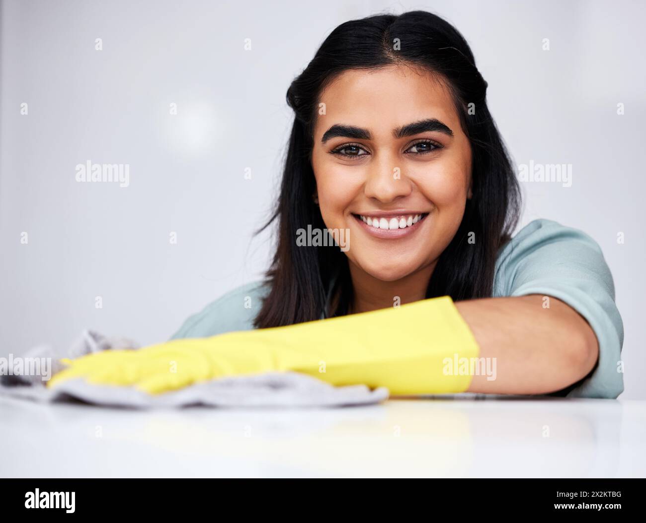 Donna indiana, ritratto o detergente con flacone spray per tavolo, cucina o mobili sporchi in casa. Sorridi, cameriera o cameriera che lavava in disordine Foto Stock