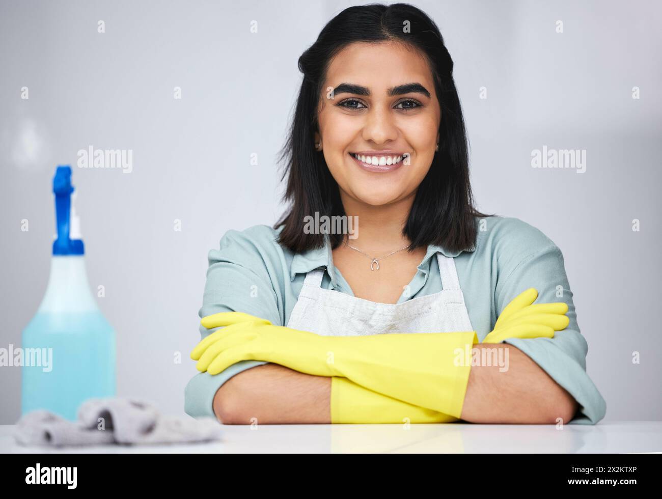 Ritratto, donna indiana e detergente con sorriso o flacone spray per tavolo, bancone o mobili sporchi in casa. Braccia incrociate, cameriera o custode orgoglioso Foto Stock