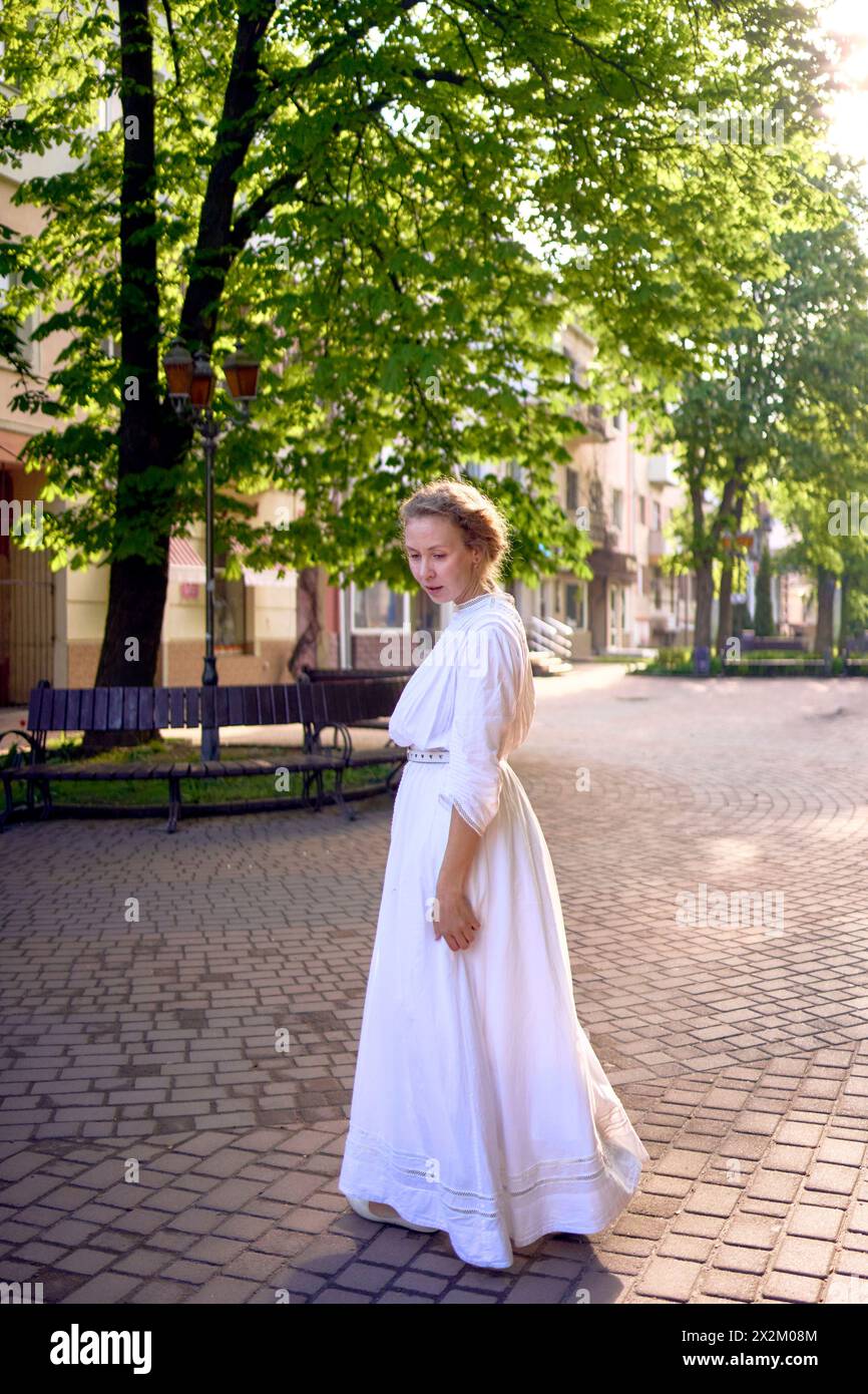 elegante donna di mezza età con un abito vintage bianco in un vicolo illuminato dal sole Foto Stock
