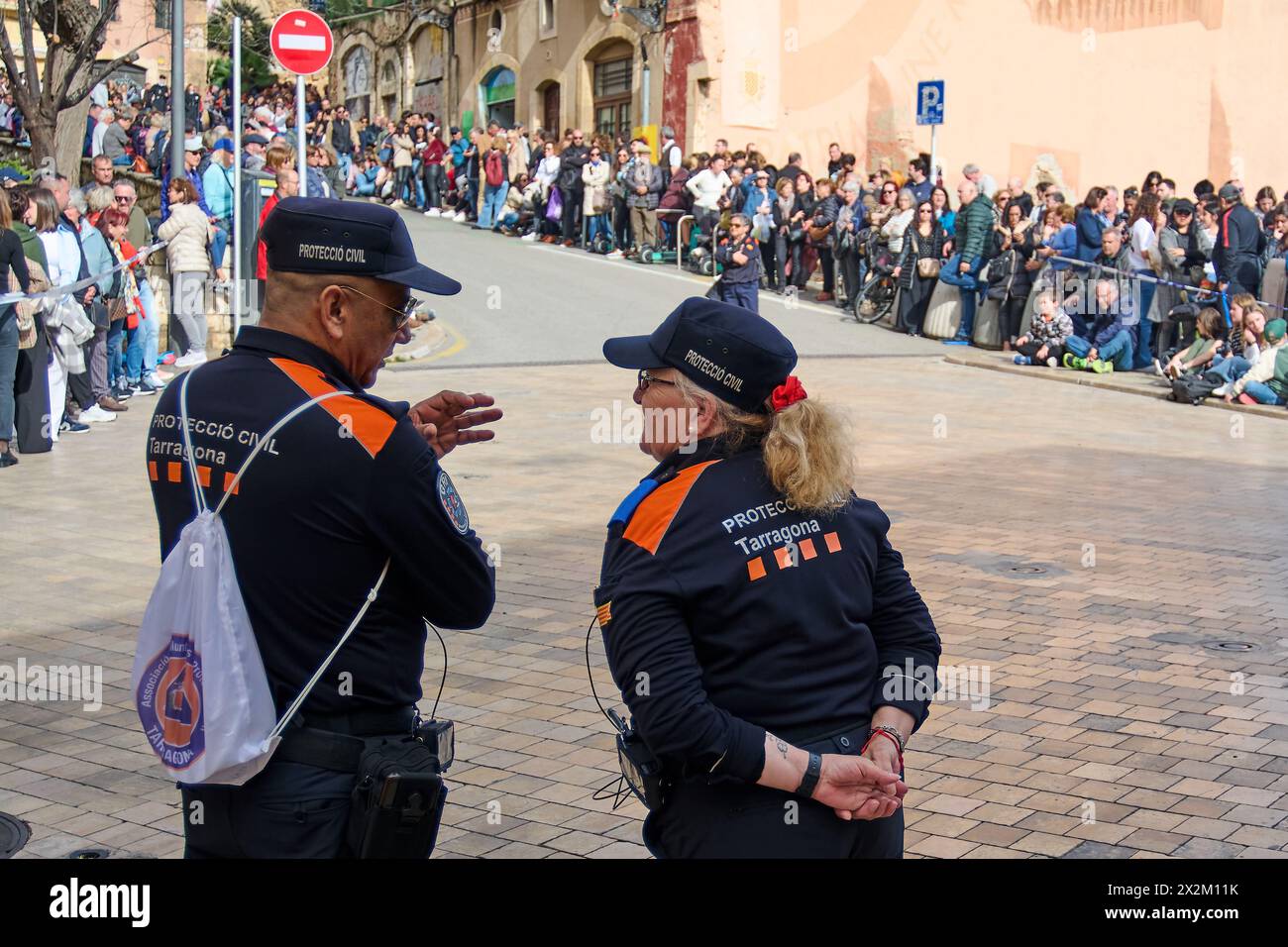 Tarragona, Spagna - 23 aprile 2024: Due ufficiali della protezione civile sul retro sorvegliano la folla durante un evento all'aperto in una strada trafficata, garantendo sicurezza Foto Stock