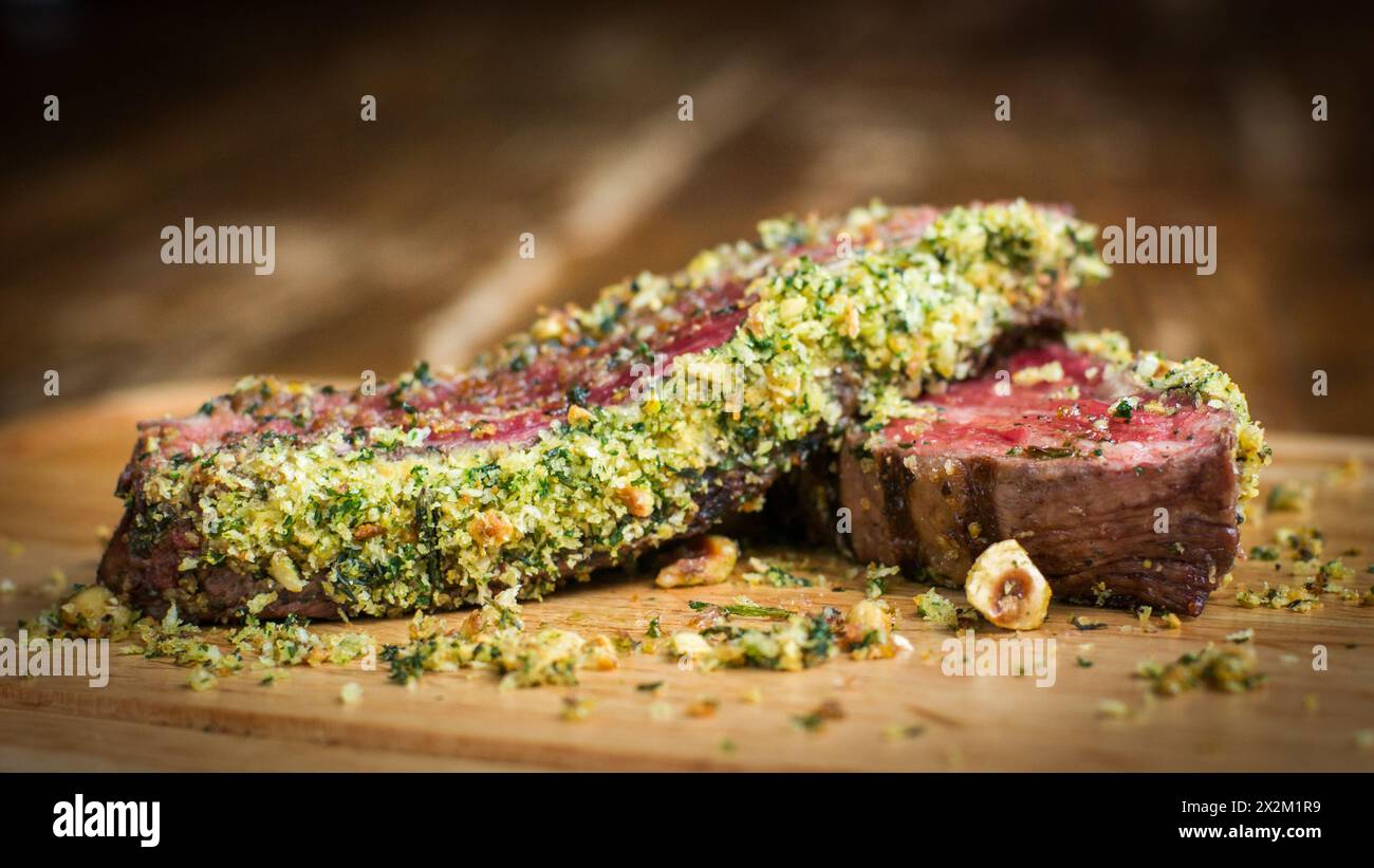 Bistecca di fianco con crosta di nocciole ed erbe aromatiche su tavola di legno in un ristorante Foto Stock