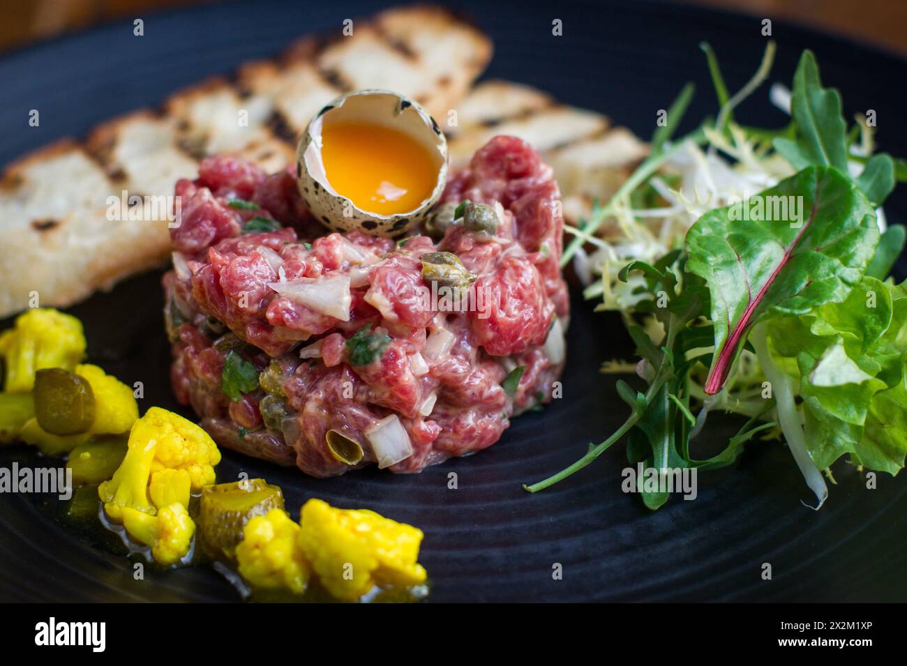 Tartare di bistecca con uovo di quaglia, toast e piccalilli sul piatto in un ristorante Foto Stock