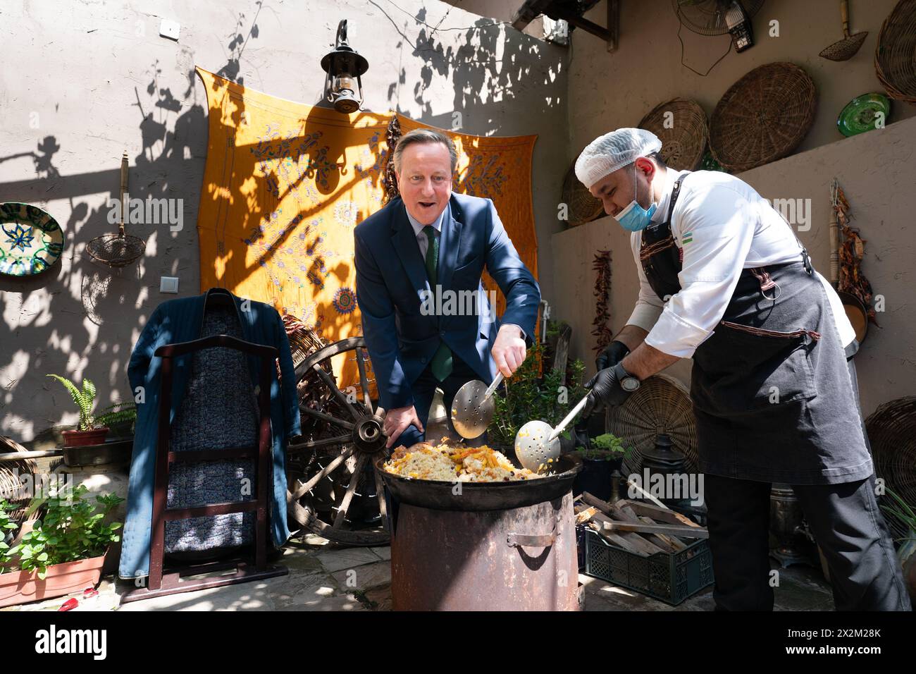 Il Segretario degli Esteri Lord David Cameron (a sinistra) mescola una pentola di Plov uzbeko al ristorante Caravan di Tashkent, mentre visita l'Uzbekistan durante il suo tour di cinque giorni nella regione dell'Asia centrale. Data foto: Martedì 23 aprile 2024. Foto Stock