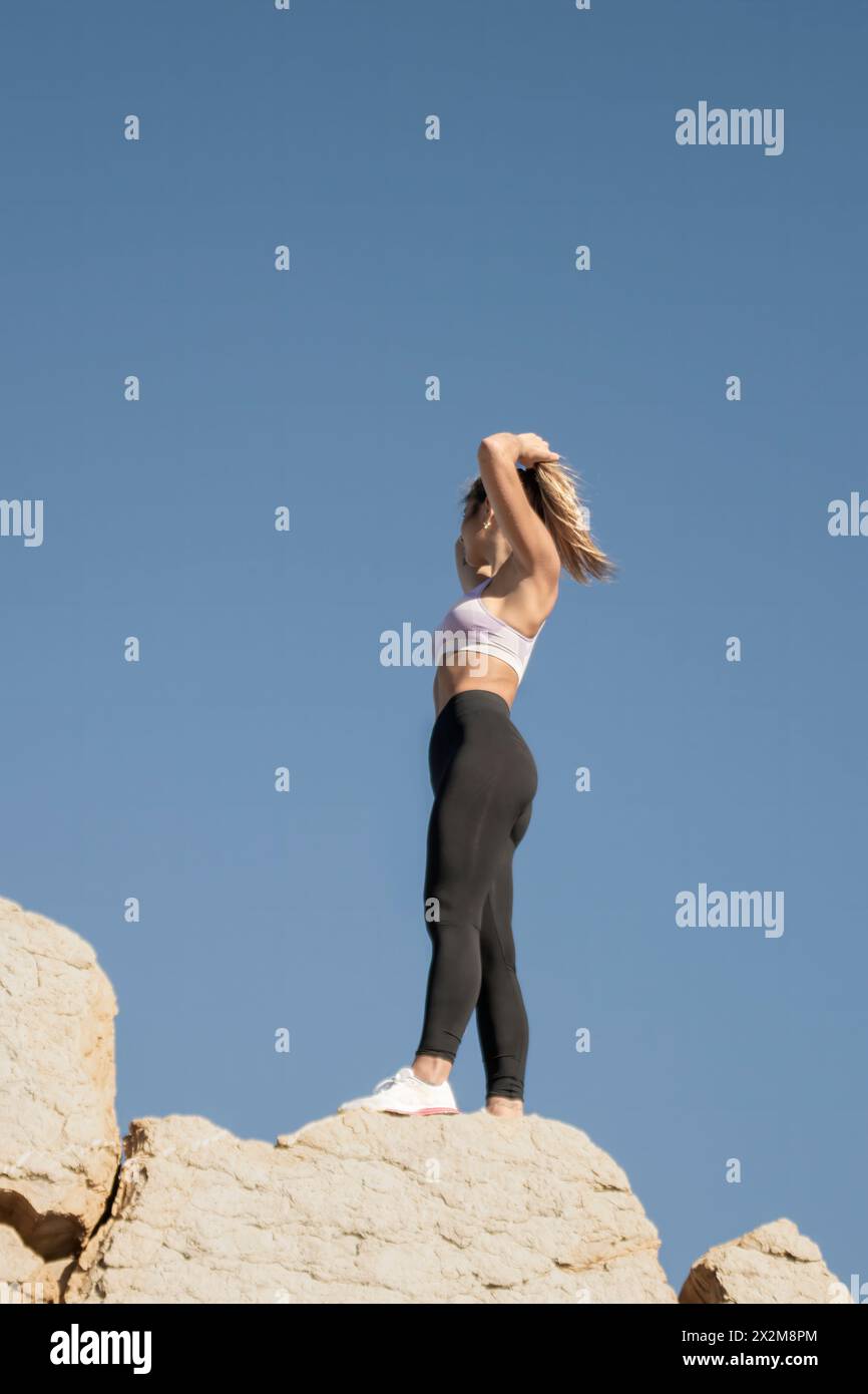 donna sportiva dinamica sullo sfondo di rocce contrastanti, sotto un cielo limpido, che evoca libertà e movimento Foto Stock