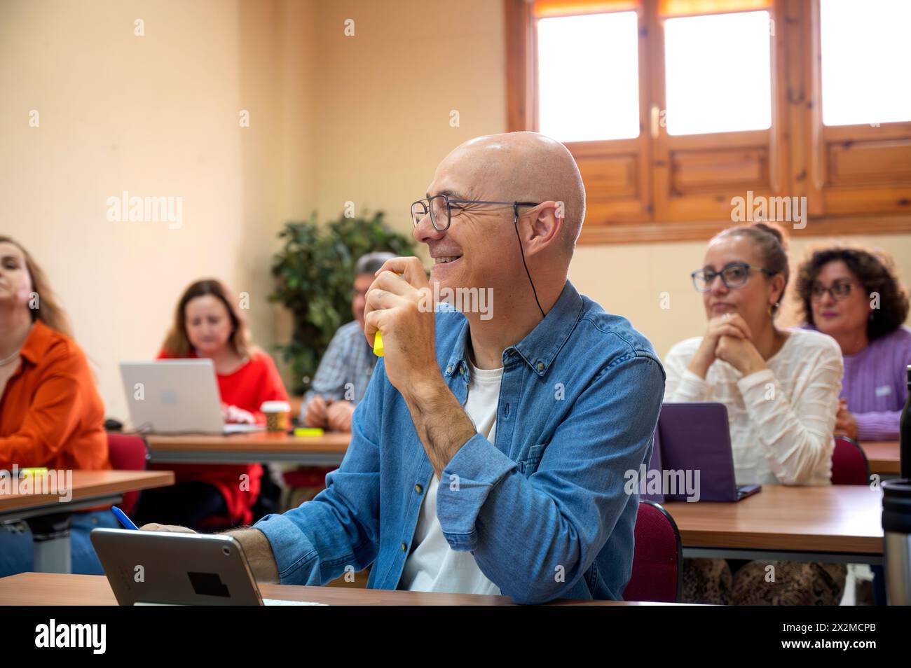 Un anziano sorridente che partecipa a una sessione di apprendimento con i colleghi in un ambiente scolastico, mostrando la gioia di continuare a studiare Foto Stock
