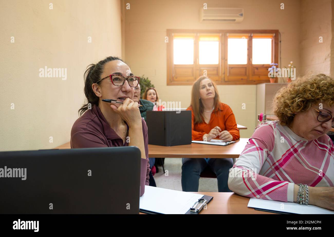 Una donna matura attenta che partecipa a una lezione in classe con altri studenti adulti impegnati nell'istruzione Foto Stock
