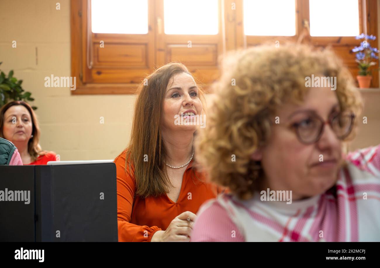 Un gruppo di donne adulte attente che imparano in aula, si è concentrato sull'acquisizione di nuove competenze con un notebook visibile Foto Stock