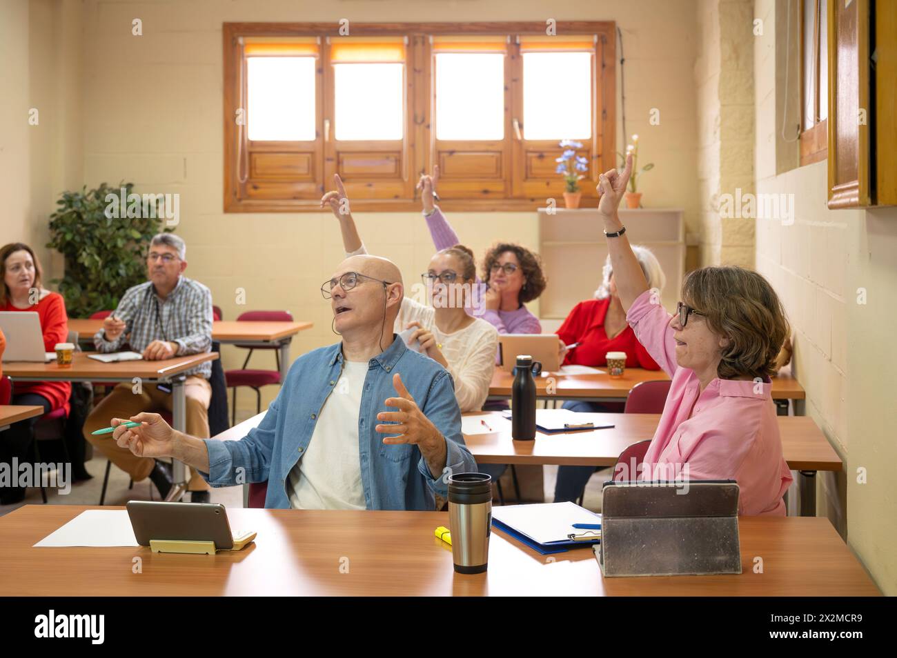 Adulti anziani entusiasti che partecipano attivamente a un'aula, con un individuo che alza con ansia la mano Foto Stock