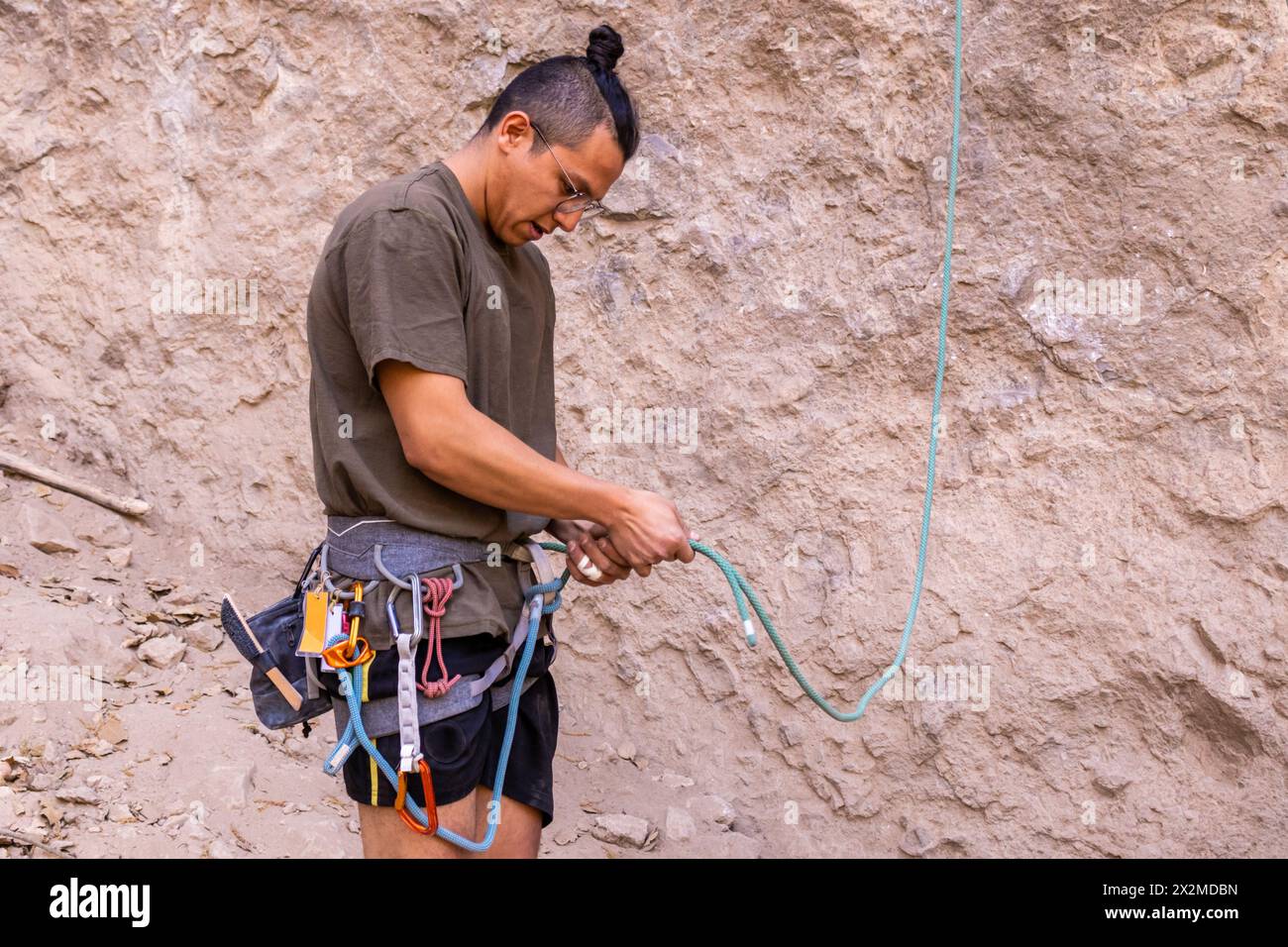 Un scalatore attento controlla la corda e le attrezzature su uno sfondo roccioso, mettendo in evidenza la sicurezza negli sport di arrampicata Foto Stock