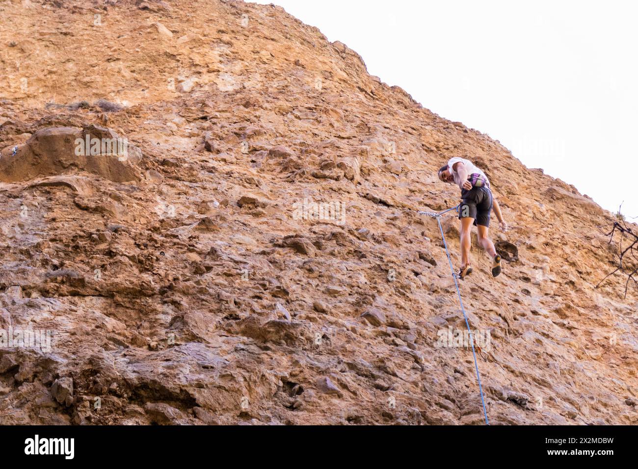 Un arrampicatore sale su una ripida parete rocciosa, fissando le corde lungo l'aspra via di arrampicata Foto Stock