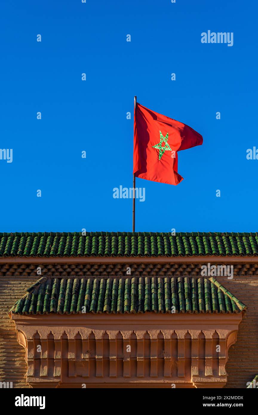 La vibrante bandiera marocchina fluttua orgogliosamente in un cielo senza nuvole sopra un edificio che mostra la tradizionale architettura marocchina. Foto Stock