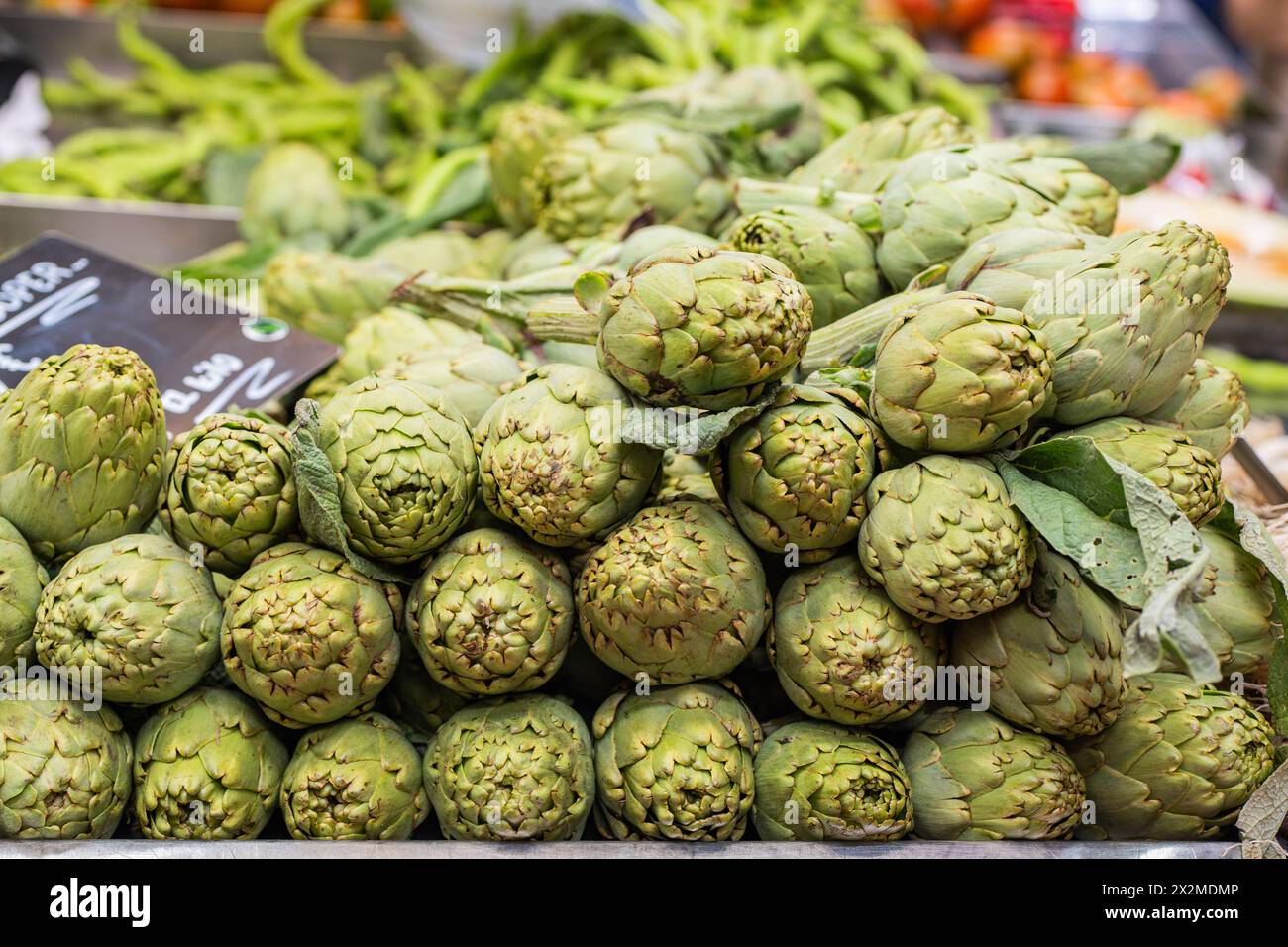 Mazzo di carciofi verdi freschi in vendita presso un mercato agricolo locale con un cartello di prezzo Foto Stock