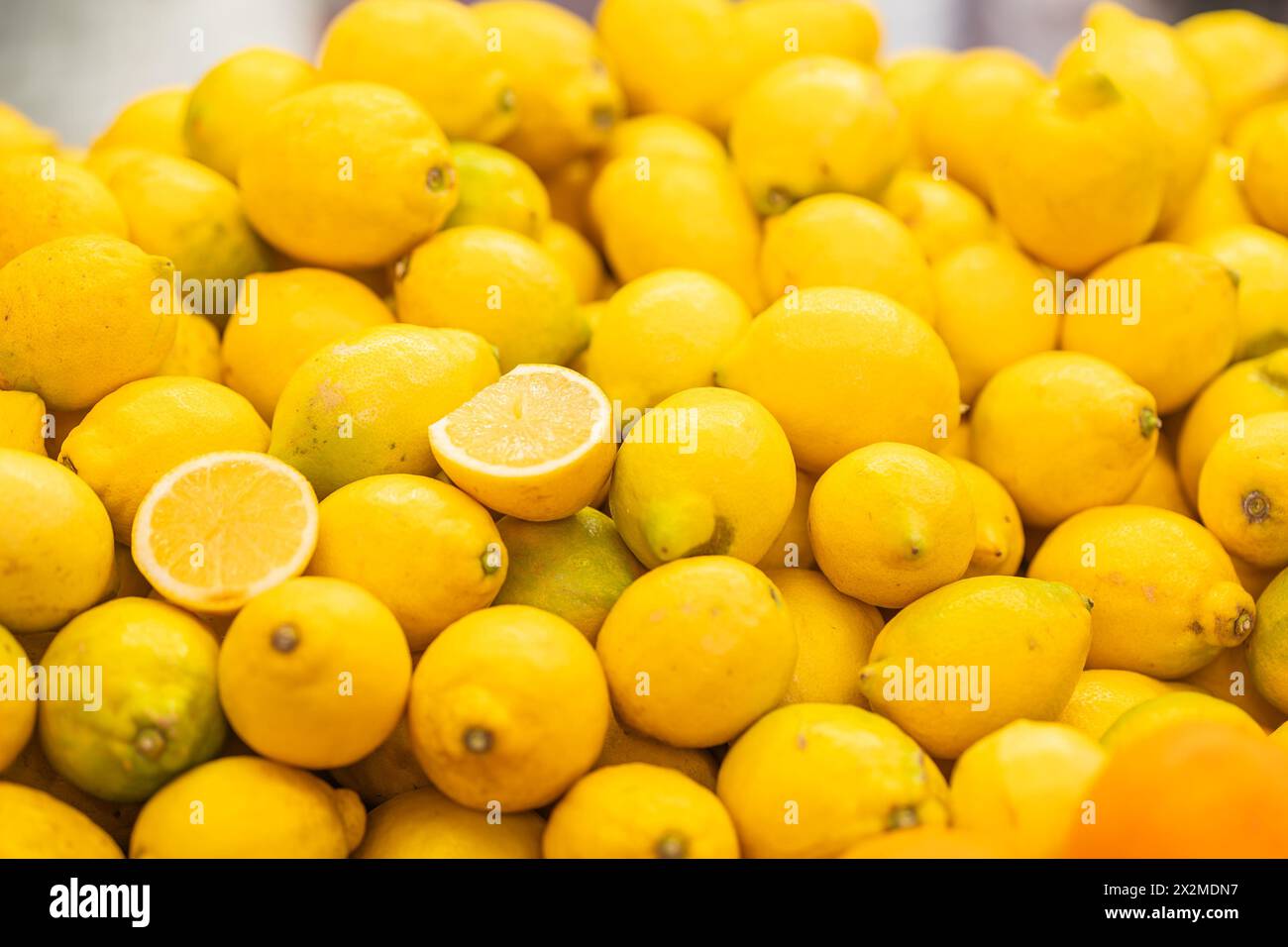 Un vivace mucchio di limoni freschi e maturi con un solo limone tagliato a metà, che ne mostra il succoso interno Foto Stock