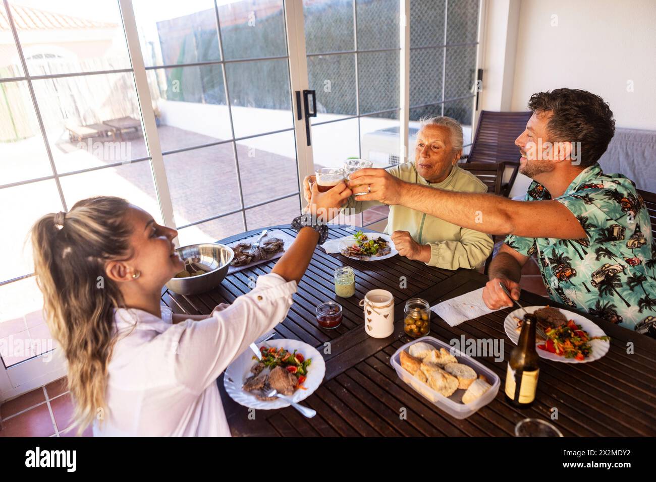 Una donna anziana, un giovane uomo e una donna si godono un momento di connessione a un barbecue nel cortile Foto Stock