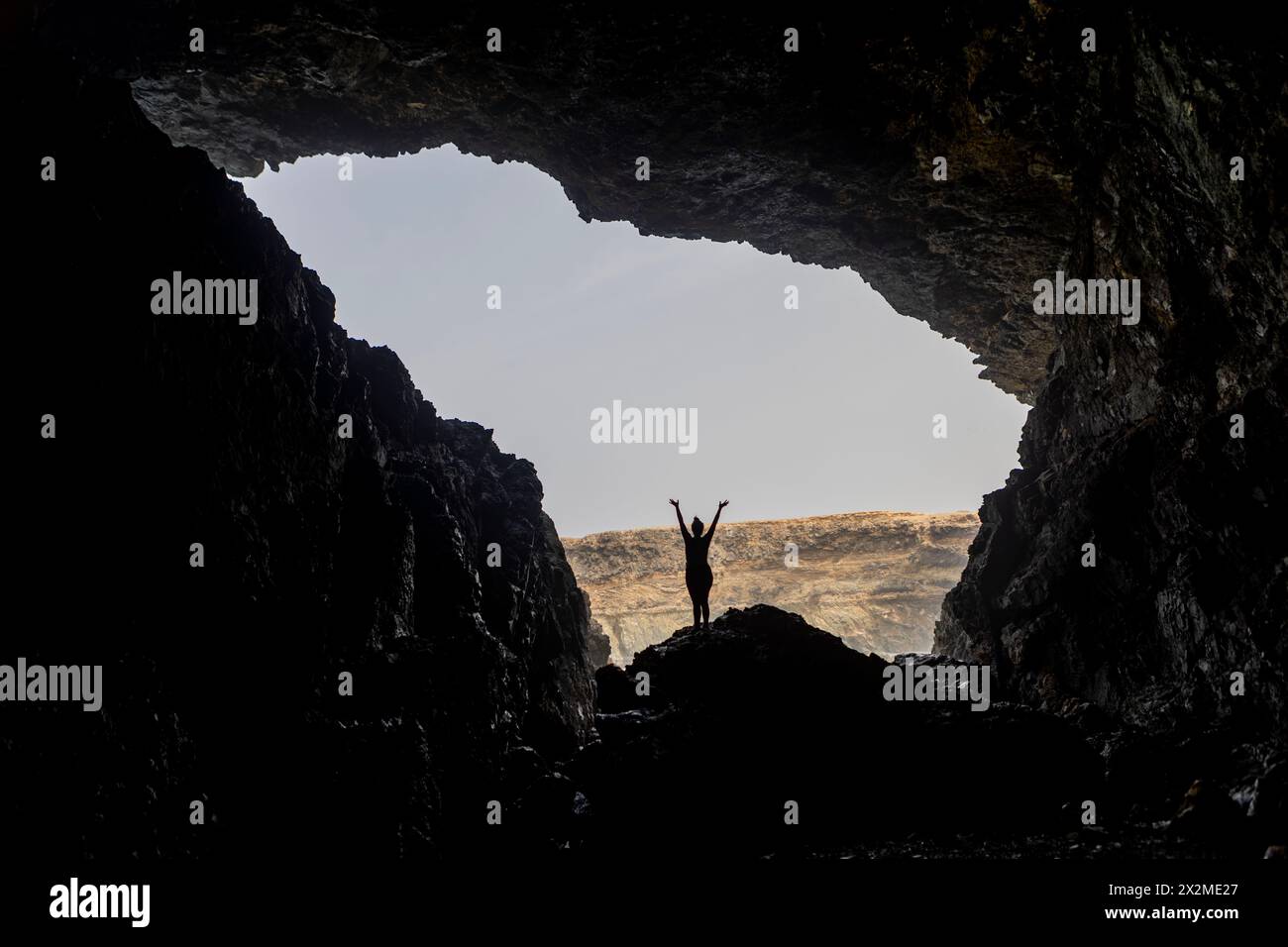 Silhouette di una donna eccezionale e irriconoscibile con le braccia alzate in una grotta aperta durante un'escursione a Fuerteventura, nelle Isole Canarie, in Spagna. Foto Stock