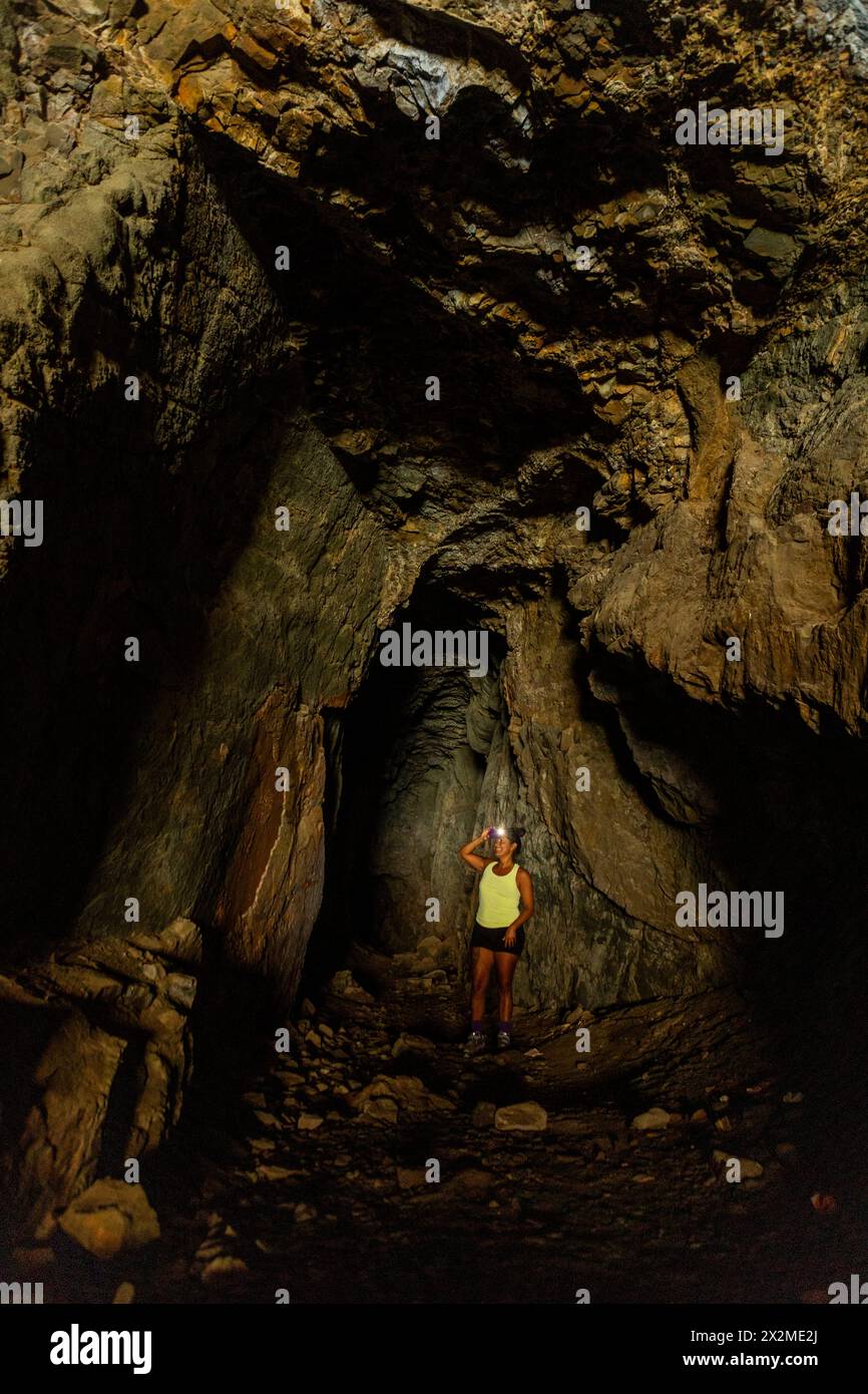 Una donna con un faro esplora la vastissima oscurità di una grotta sotterranea naturale, evidenziando le superfici rocciose intorno. Foto Stock