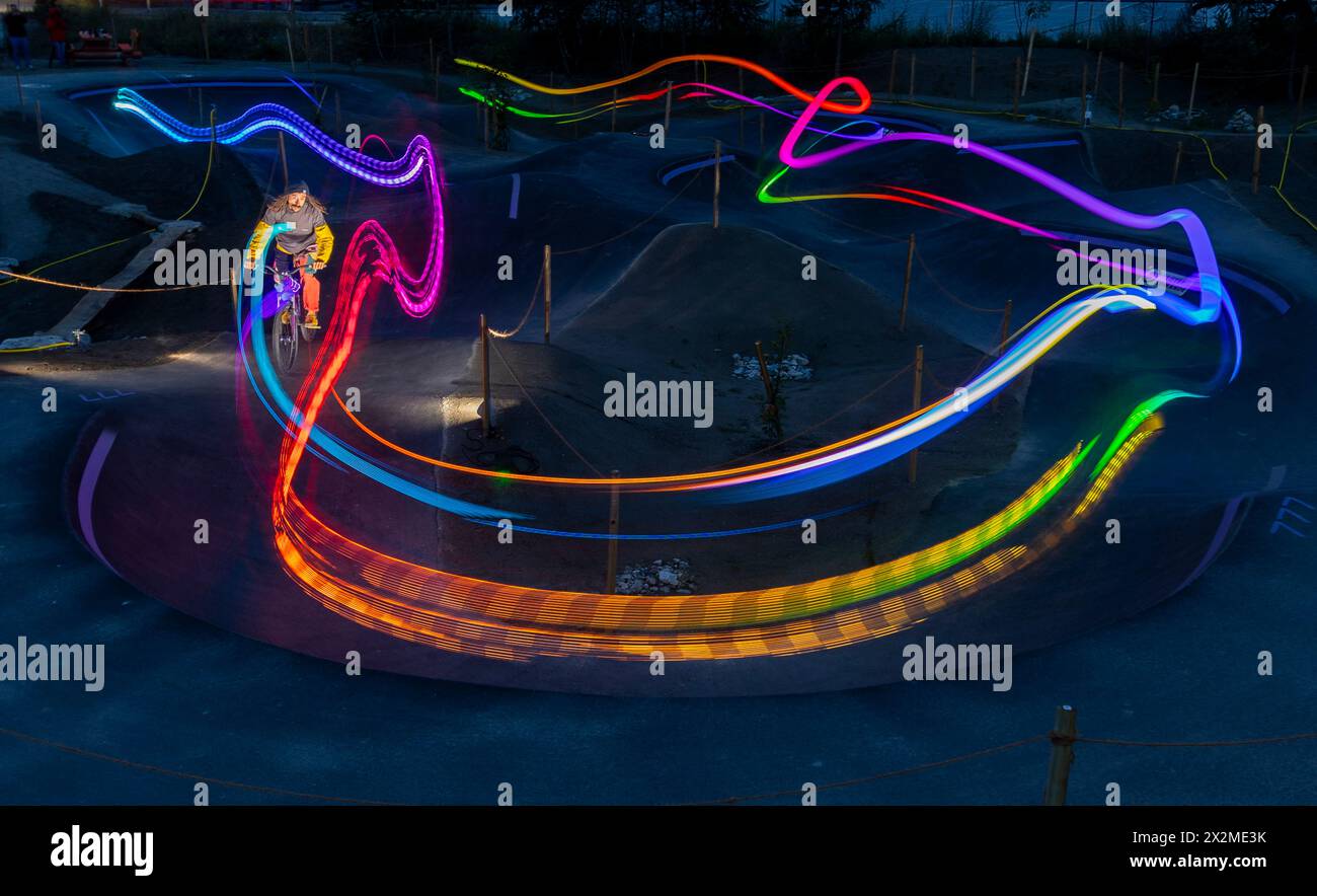 Un ciclista manovra attraverso un parcheggio per biciclette di notte, lasciando una vivace scia di luci colorate in una lunga fotografia Foto Stock