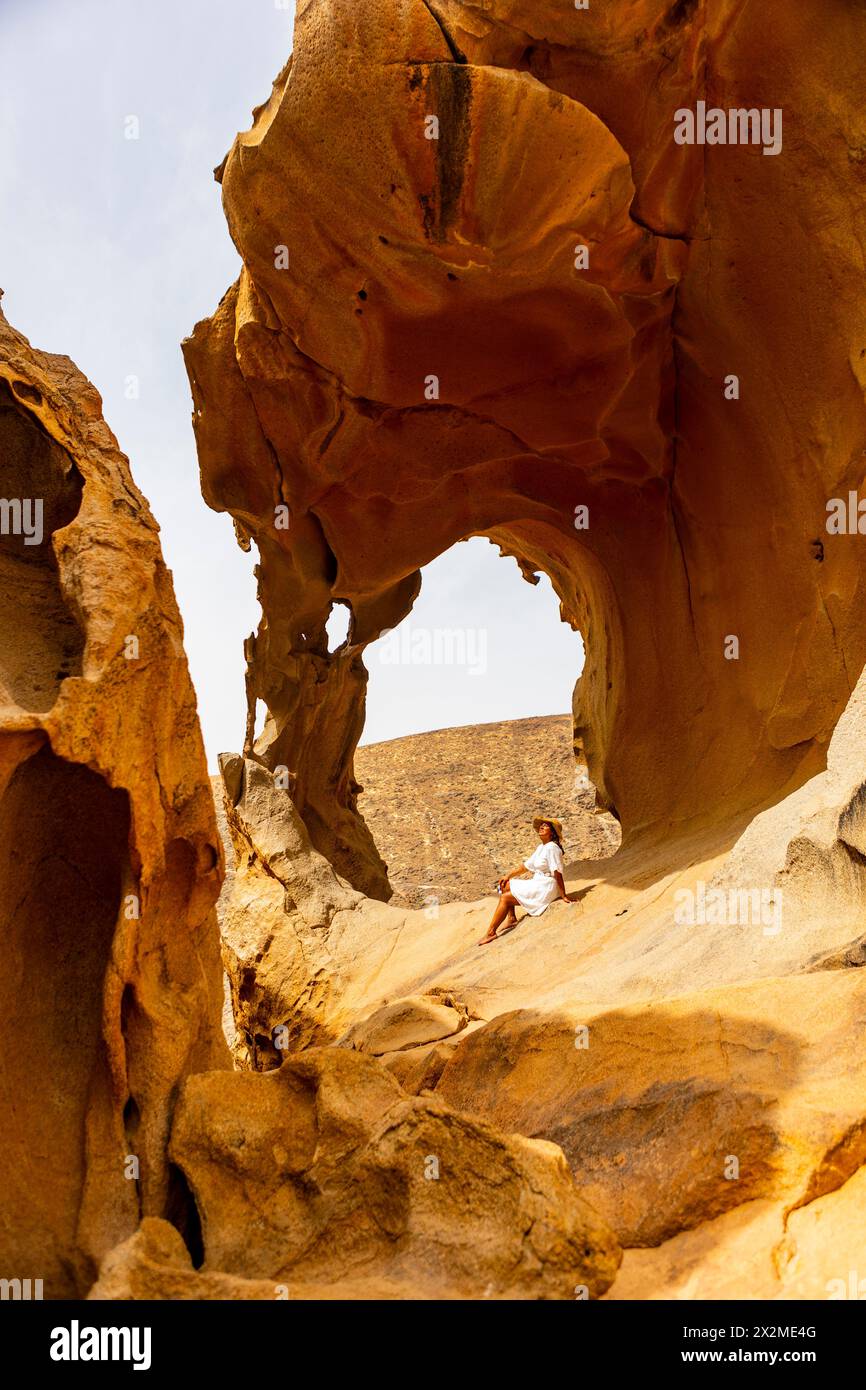 Una donna con un abito bianco trova una tranquilla fuga seduto tra rocce intemprate in un ambiente naturale desertico. Foto Stock