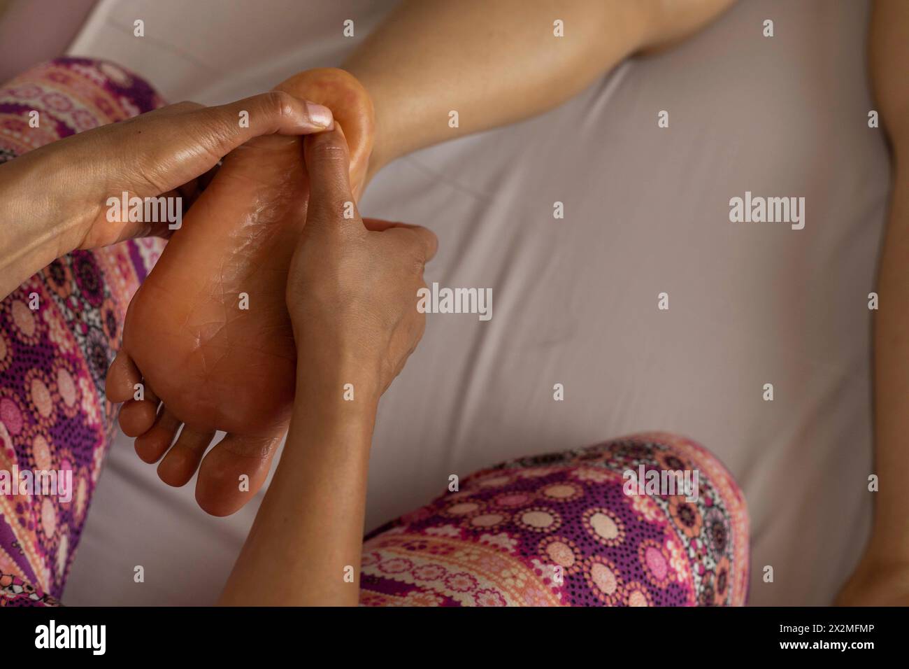 Una donna latina sdraiata sulla schiena riceve un massaggio ayurvedico sul piede, nelle mani in primo piano di una massaggiatrice donna. Conce per massaggio curativo Foto Stock