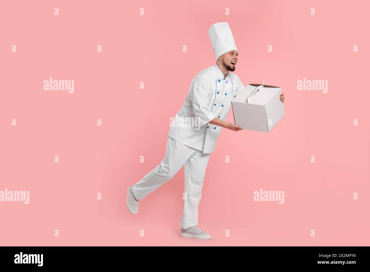 Dolcificante professionale felice in scatola per torte in uniforme su sfondo rosa Foto Stock