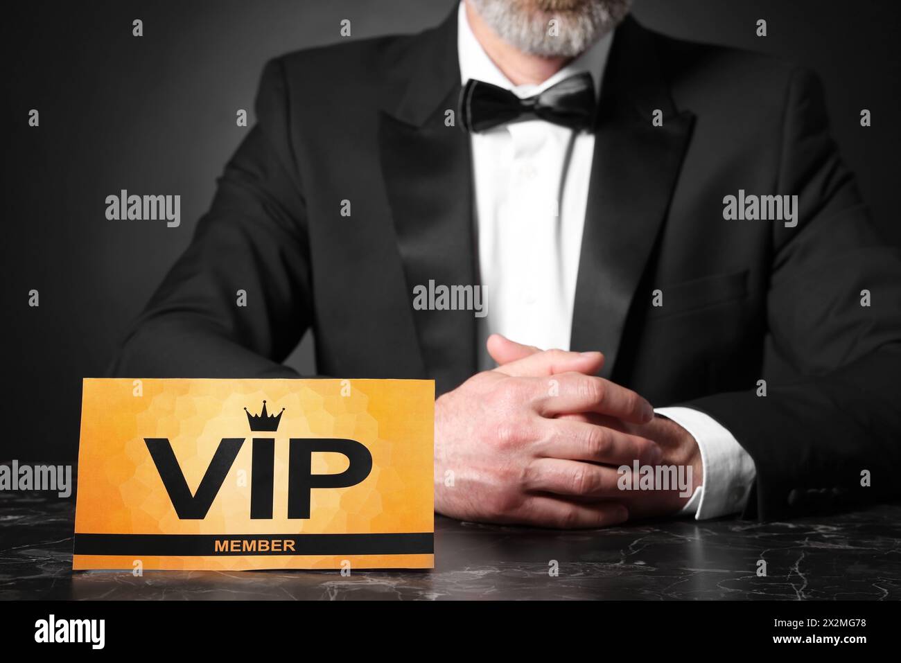Uomo seduto al tavolo con un cartello VIP su sfondo nero, primo piano Foto Stock