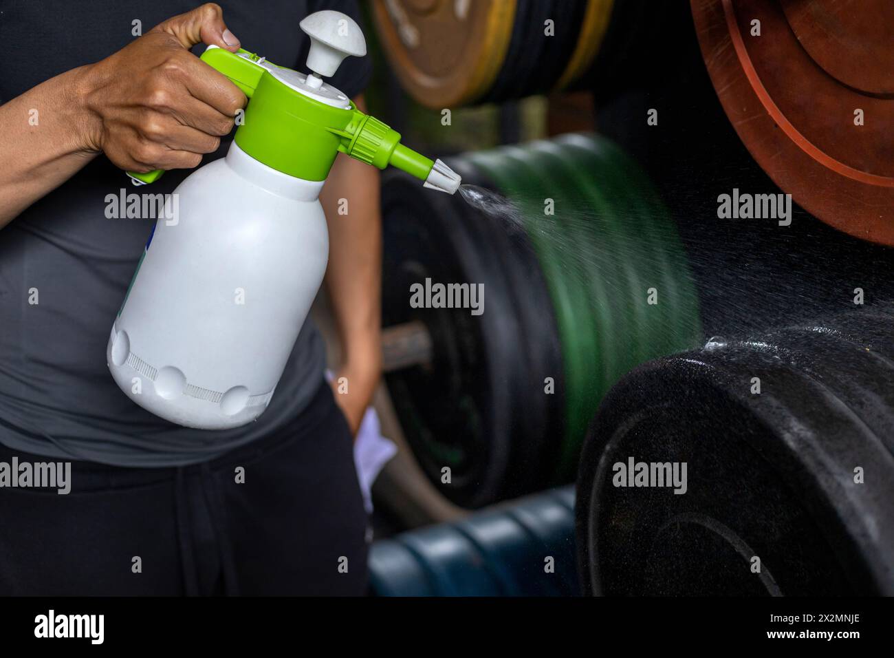 Primo piano delle mani di un uomo utilizzando una bottiglia di disinfettante per pulire i dischi di peso in palestra. Concetto di disinfezione, pulizia, antibatterico Foto Stock