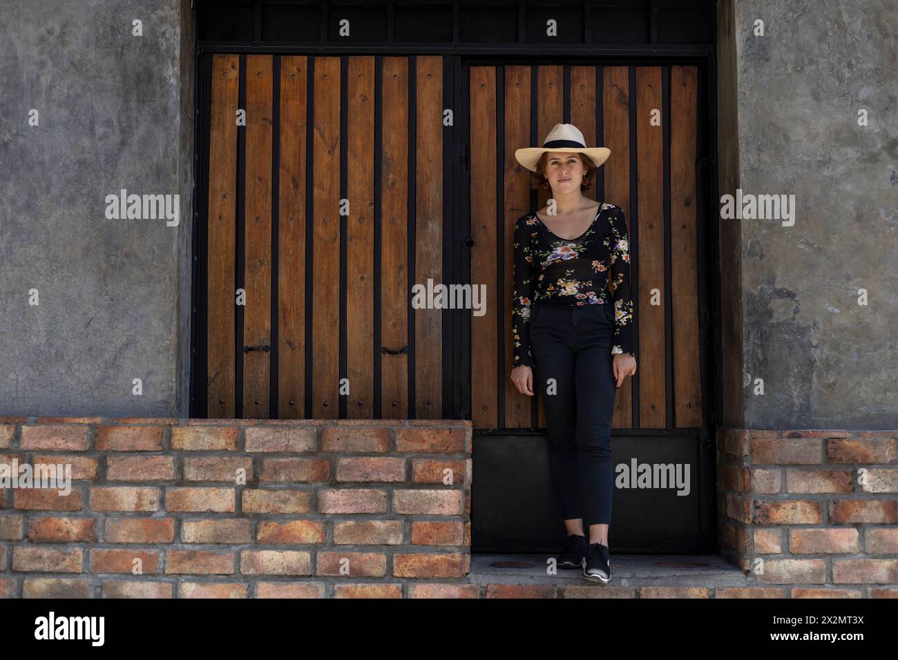 Giovane ragazza latino-americana (22) con cappello da cowboy posa davanti all'ingresso in legno sullo sfondo. Copia spazio. Concetto del modello Foto Stock