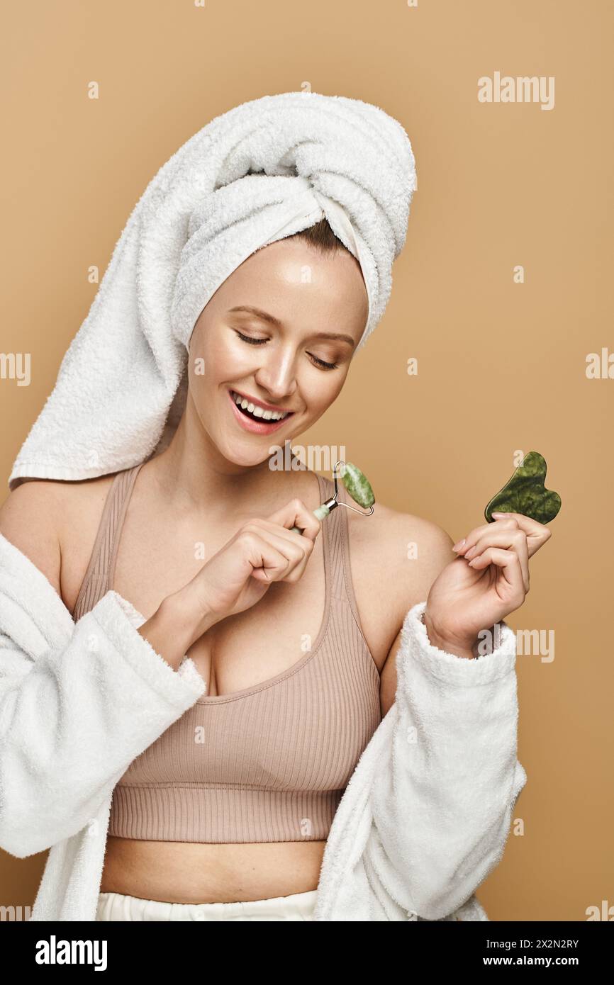 Una donna con un asciugamano sulla testa tiene il rullo facciale, mostrando bellezza naturale e un legame con una sana alimentazione. Foto Stock