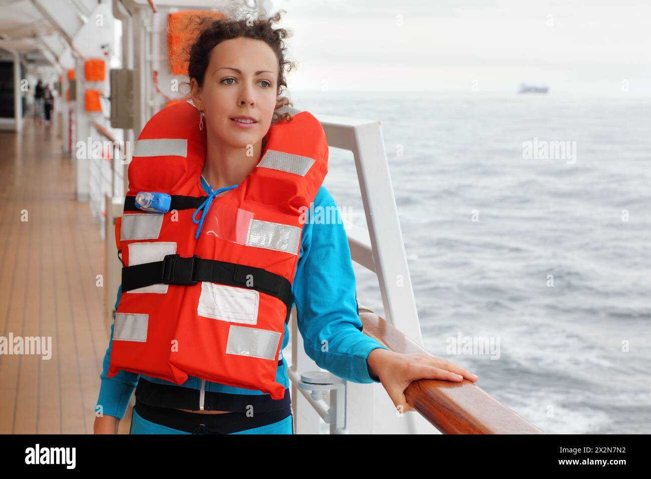 Una bella donna che indossa un giubbotto salvagente arancione guarda in lontananza sul ponte della nave Foto Stock
