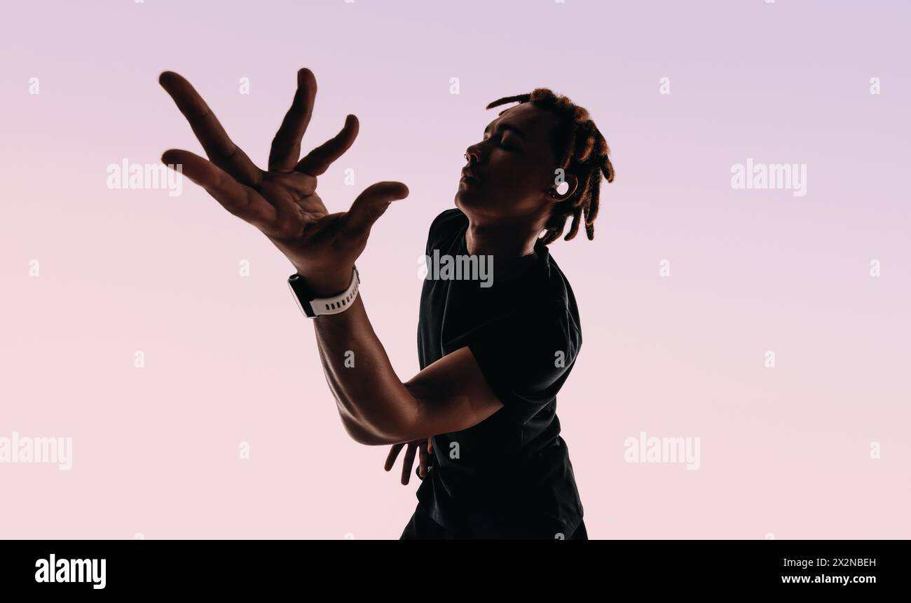 Giovane espressivo con dreadlocks danzano energicamente in studio al ritmo di una canzone. Ha gli occhi chiusi, le mani in movimento, ascolta con wirel Foto Stock