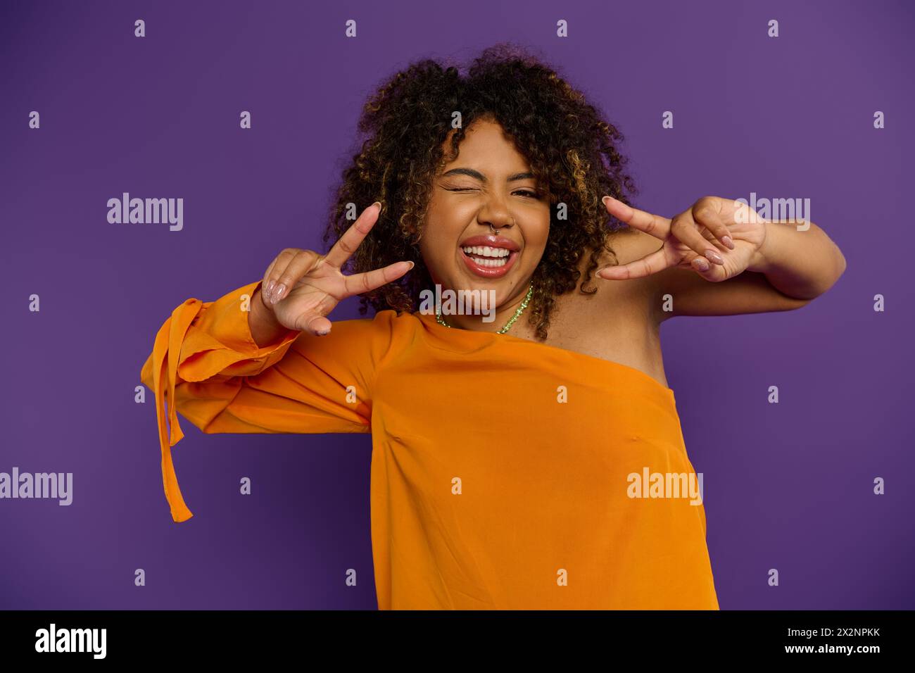 Una donna afroamericana in cima arancione colpisce un gesto di pace. Foto Stock