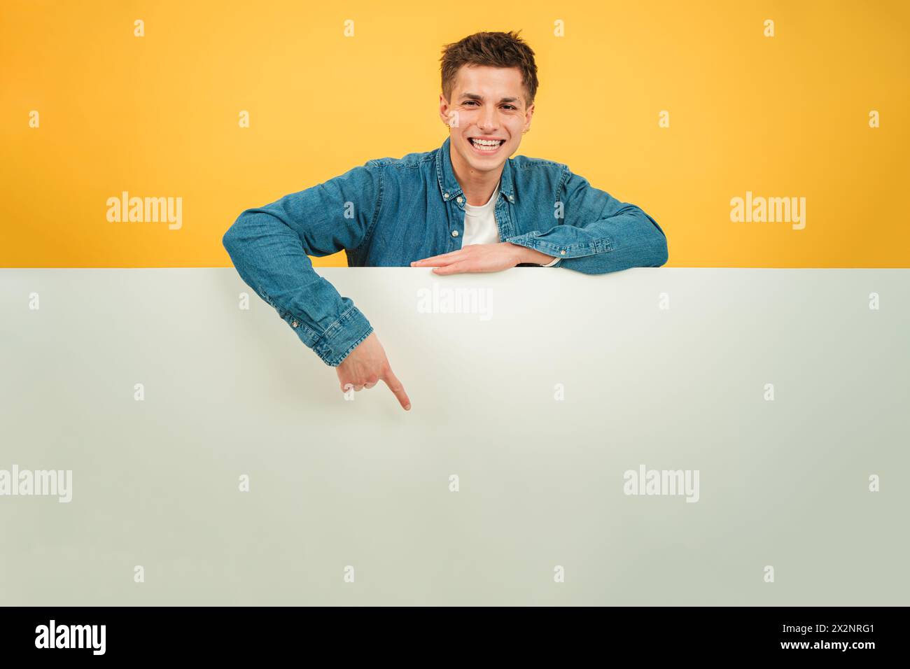 Giovane uomo caucasico che punta una tavola vuota sullo sfondo rosso. Si consiglia di copiare il modello dello spazio. Ragazzo adolescente che mostra un copyspace per affissioni in basso su una parete di sfondo di colore giallo. Uomo che presenta. Foto di alta qualità Foto Stock