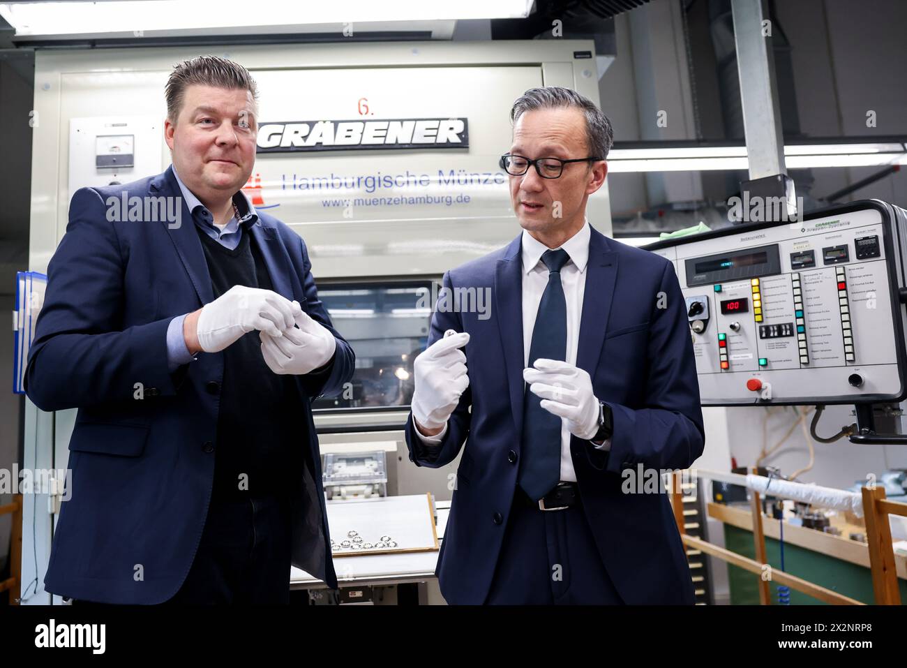 Amburgo, Germania. 23 aprile 2024. Andreas Dressel (SPD, l), senatore delle Finanze di Amburgo, e Falk Schnabel, capo della polizia di Amburgo, hanno la nuova moneta commemorativa da 10 euro "Police" di fronte a una macchina per la coniazione della zecca di Amburgo. La moneta da collezione fa parte della serie pluriennale "al servizio della società" e raffigura diversi agenti di polizia in servizio. Credito: Christian Charisius/dpa/Alamy Live News Foto Stock