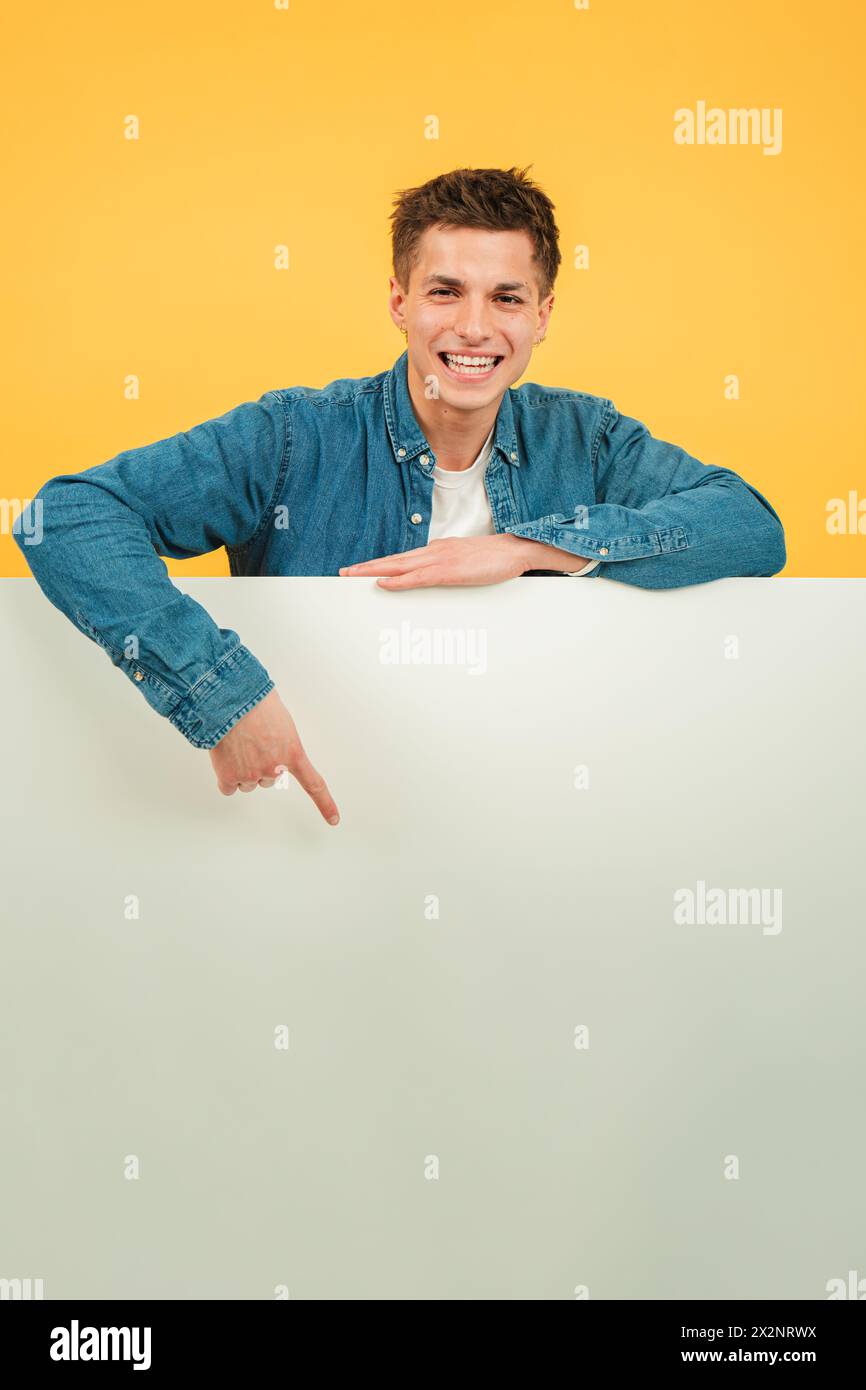 Verticale giovane uomo caucasico che punta una tavola vuota sullo sfondo rosso. Consigli per il modello di copyspace. Ragazzo adolescente che mostra un copyspace per affissioni in basso su una parete di sfondo di colore giallo. Uomo che presenta. Foto di alta qualità Foto Stock