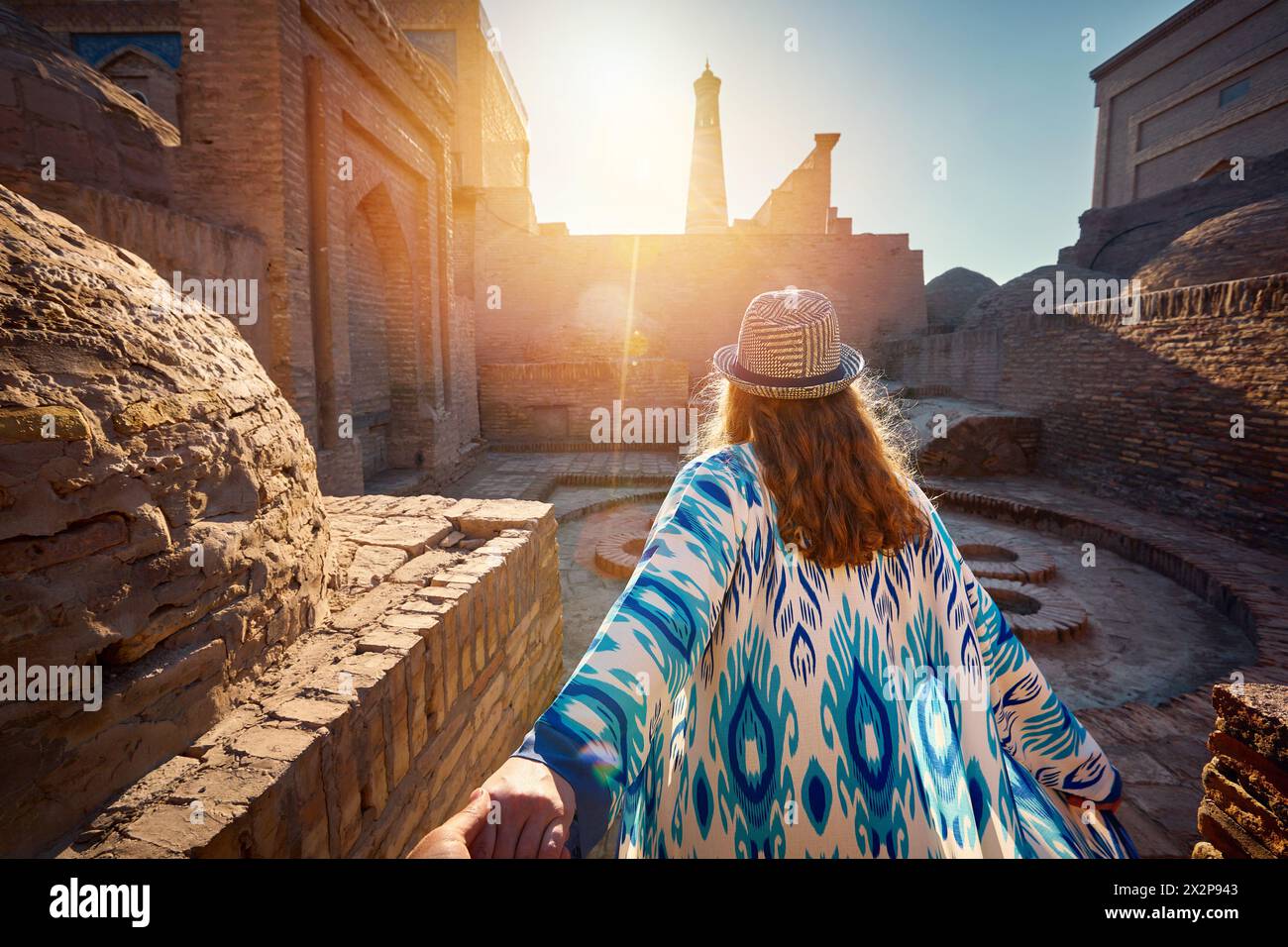 Donna turista in abito etnico presso Inner Yard vicino alla vecchia madrasa che conduce un uomo tenuto a mano presso le antiche mura della città di Khiva in Uzbekistan. Foto Stock