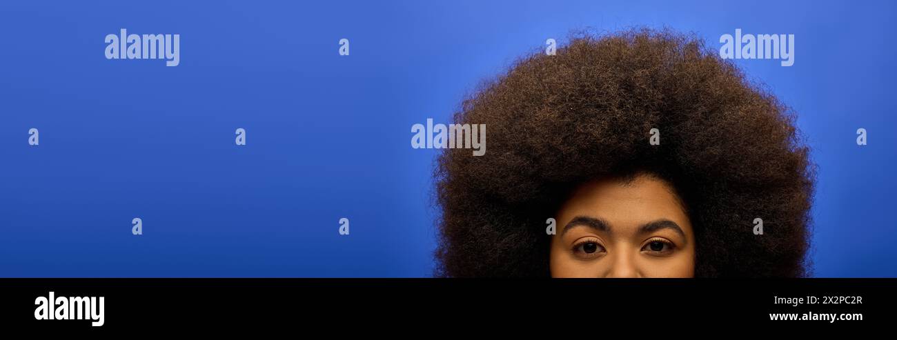 Elegante donna afroamericana in un abbigliamento alla moda che crea un volto divertente con i suoi capelli afro. Foto Stock