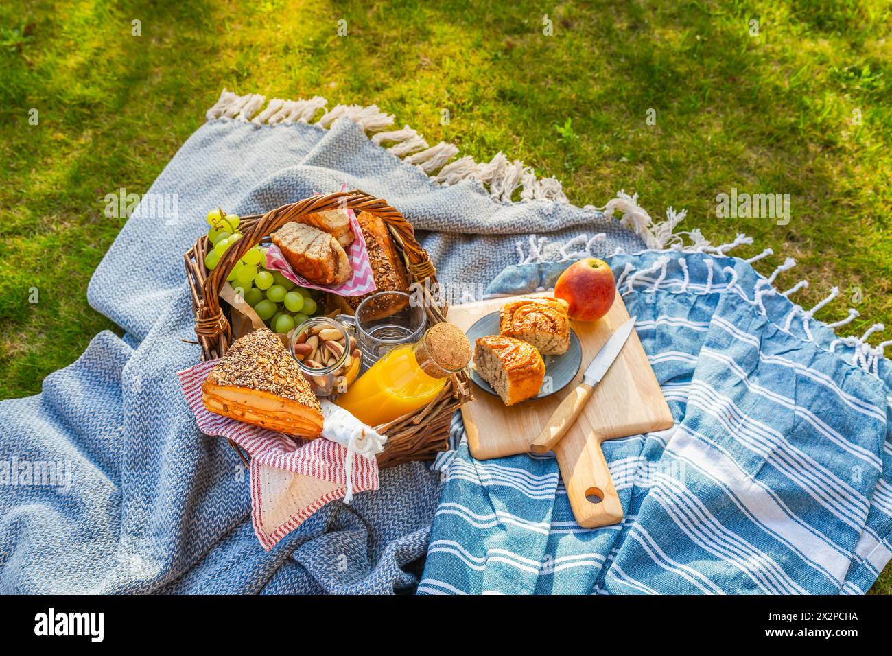 Piumino da picnic e cestino con cibi diversi, frutta, succo d'arancia, yogurt e pane su erba verde Foto Stock