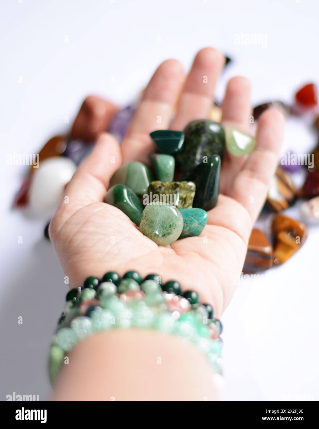 La giovane donna ha in mano una collezione di pietre preziose minerali grezze verdi che simboleggiano la guarigione, l'energia e il benessere Foto Stock