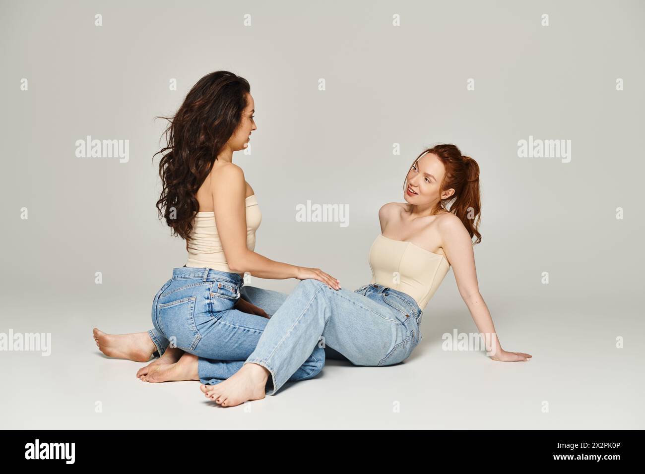 Due donne elegantemente vestite siedono a terra, invischiate in una profonda conversazione. Foto Stock