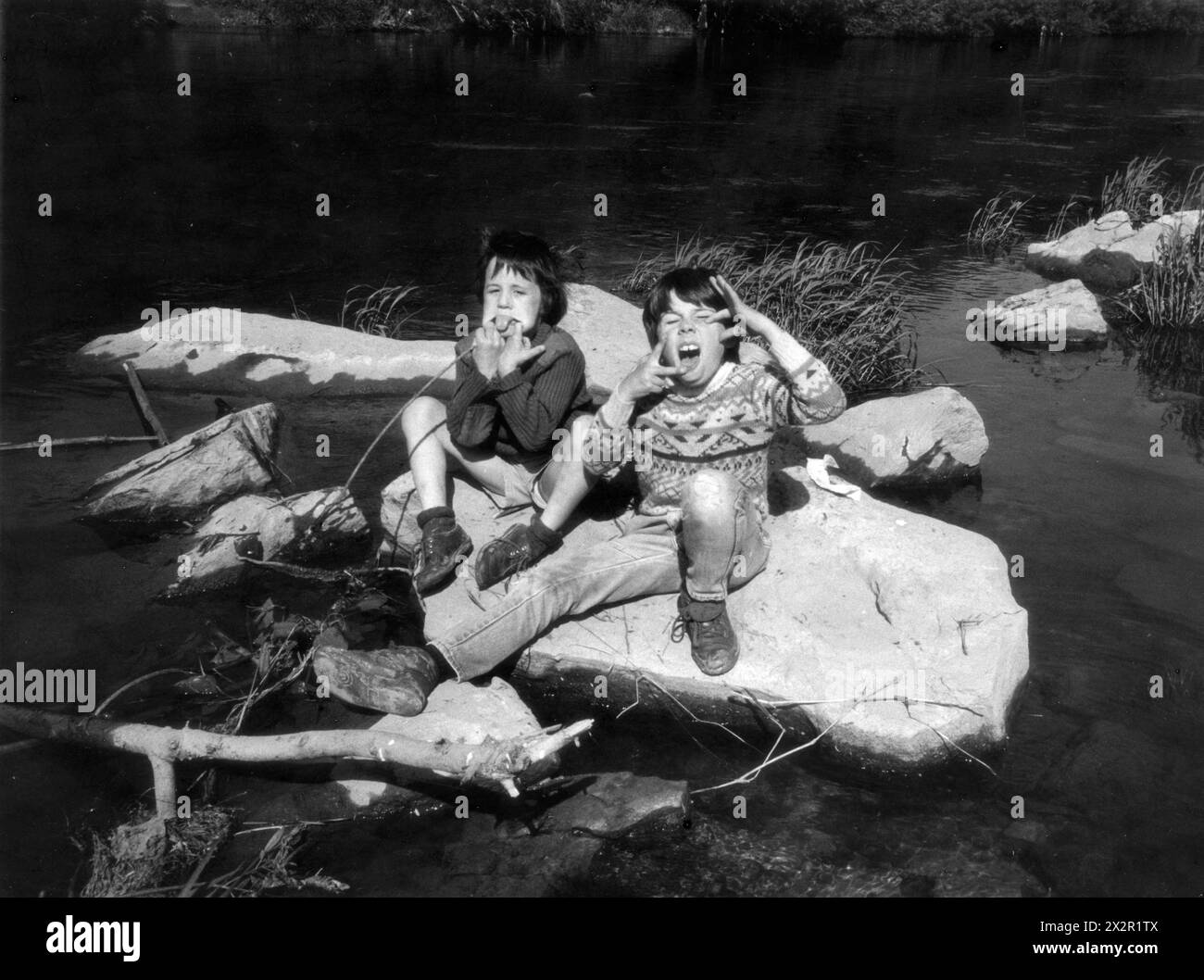 Ragazzi che giocano vicino al fiume Severn tirando espressioni facciali sfacciate Gran Bretagna 1986 Foto Stock