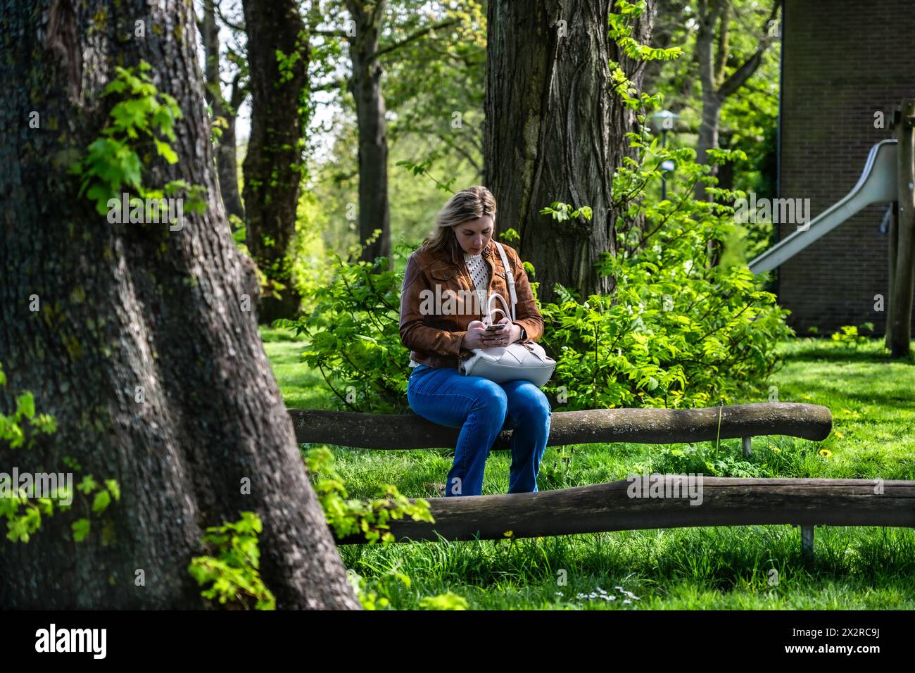Donna che lavora a distanza sul suo cellulare in un parco giochi tranquillo. Una donna seduta sulla panchina del parco, ingaggiata a inviare un'e-mail dal suo smartphone Foto Stock