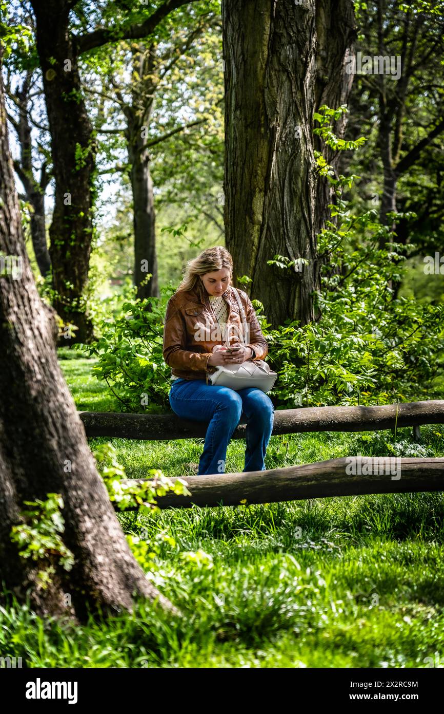 Donna attraente che lavora a distanza sul suo cellulare in un parco. Una donna seduta sulla panchina del parco, ingaggiata a inviare un'e-mail dal suo smartphone Foto Stock