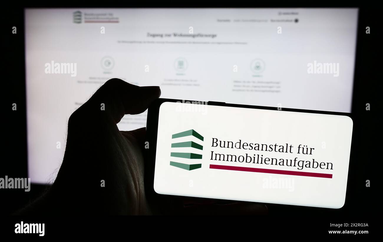 Persona che possiede un telefono cellulare con il logo dell'agenzia tedesca Bundesanstalt für Immobilienaufgaben (BIMA) di fronte alla pagina web. Mettere a fuoco il display del telefono. Foto Stock