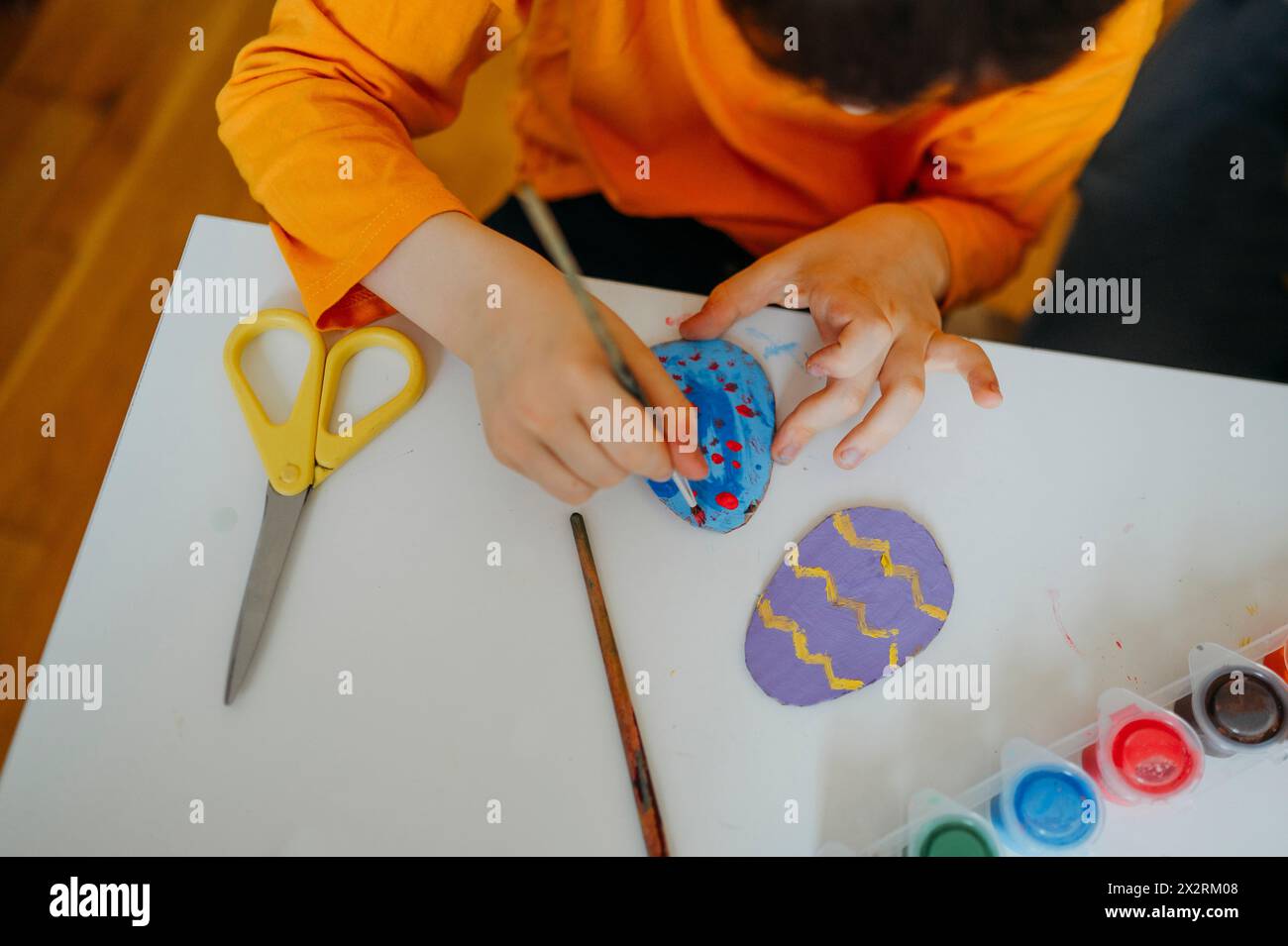 Ragazzo che dipinge uova di Pasqua in cartone a casa Foto Stock