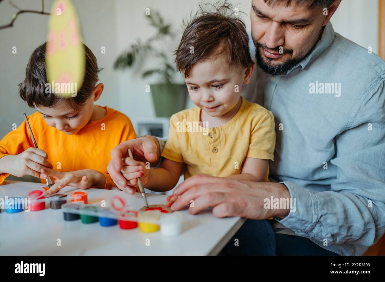 Padre con bambini che dipingono uova di Pasqua in cartone Foto Stock