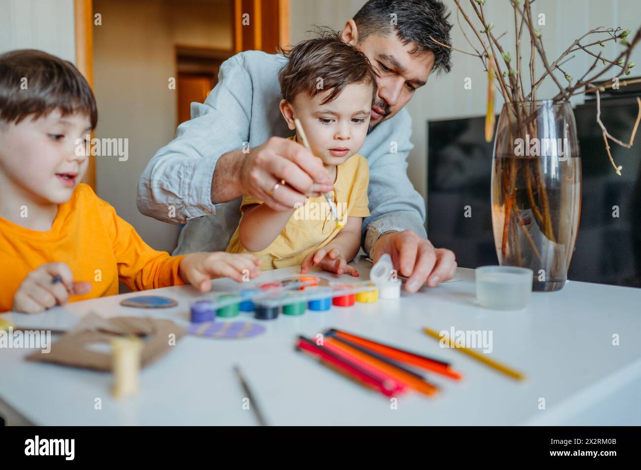 Padre con bambini che dipingono uova di Pasqua in cartone a tavola Foto Stock