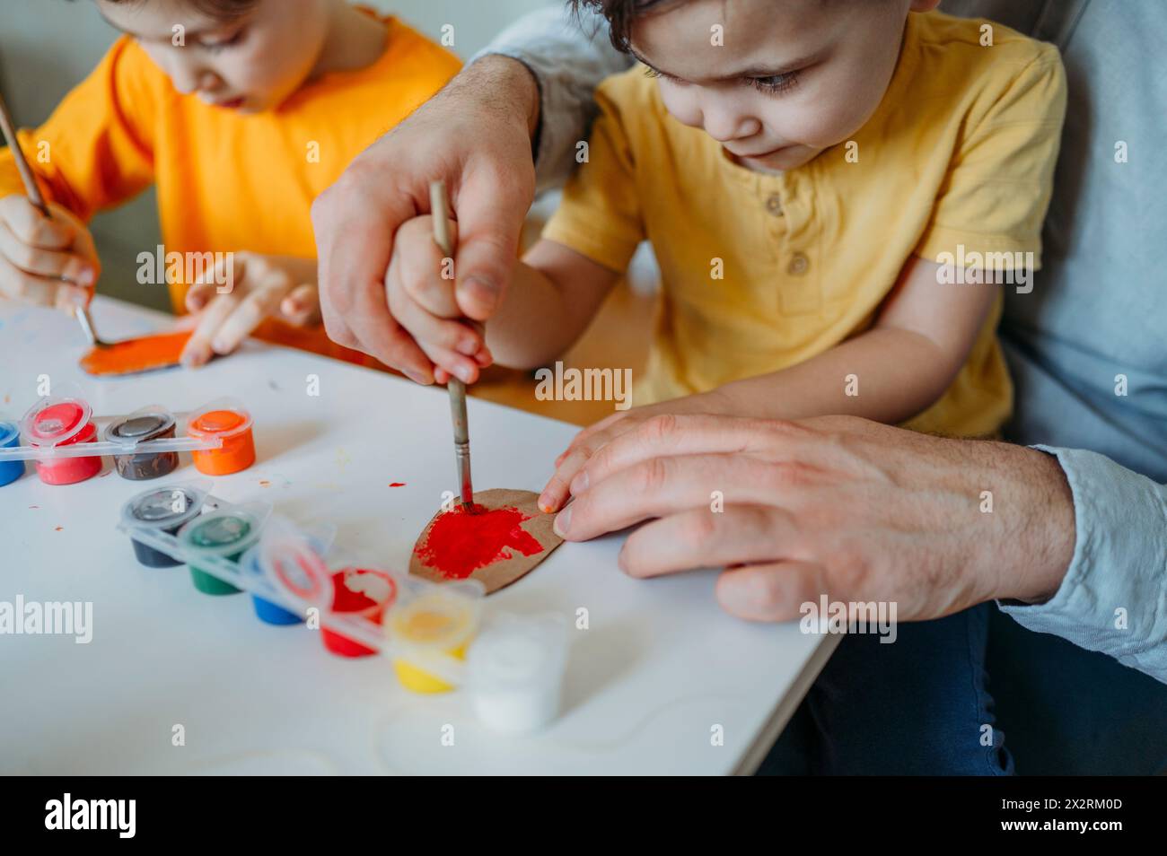 Padre e bambini dipingono uova di Pasqua in cartone a casa Foto Stock