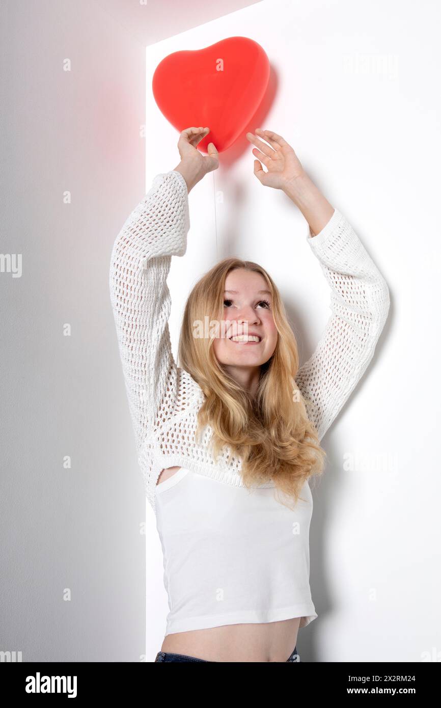 Adolescente sorridente che tiene un palloncino a forma di cuore su sfondo bianco Foto Stock